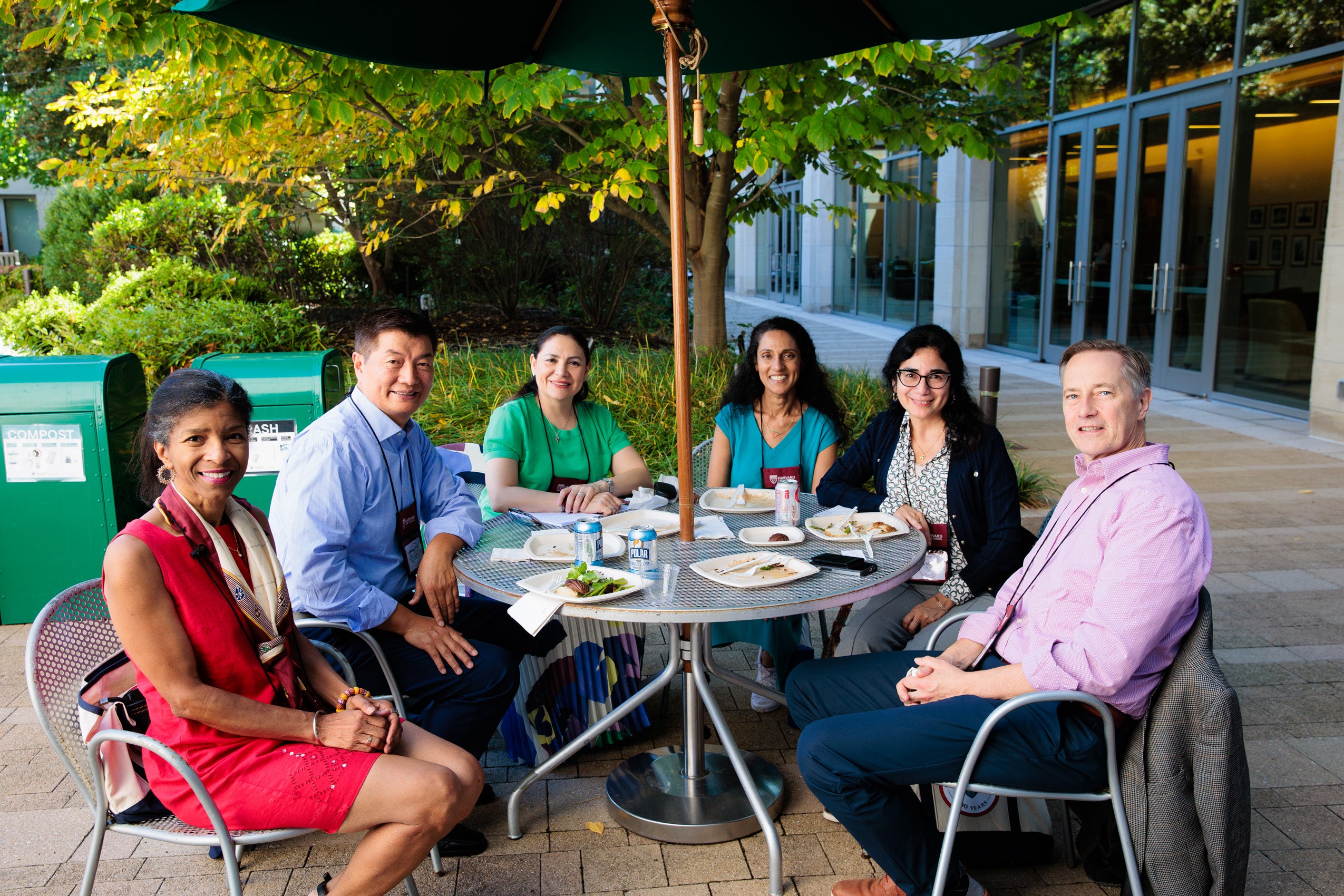 A group of people gather around a table on a patio under an umbrella