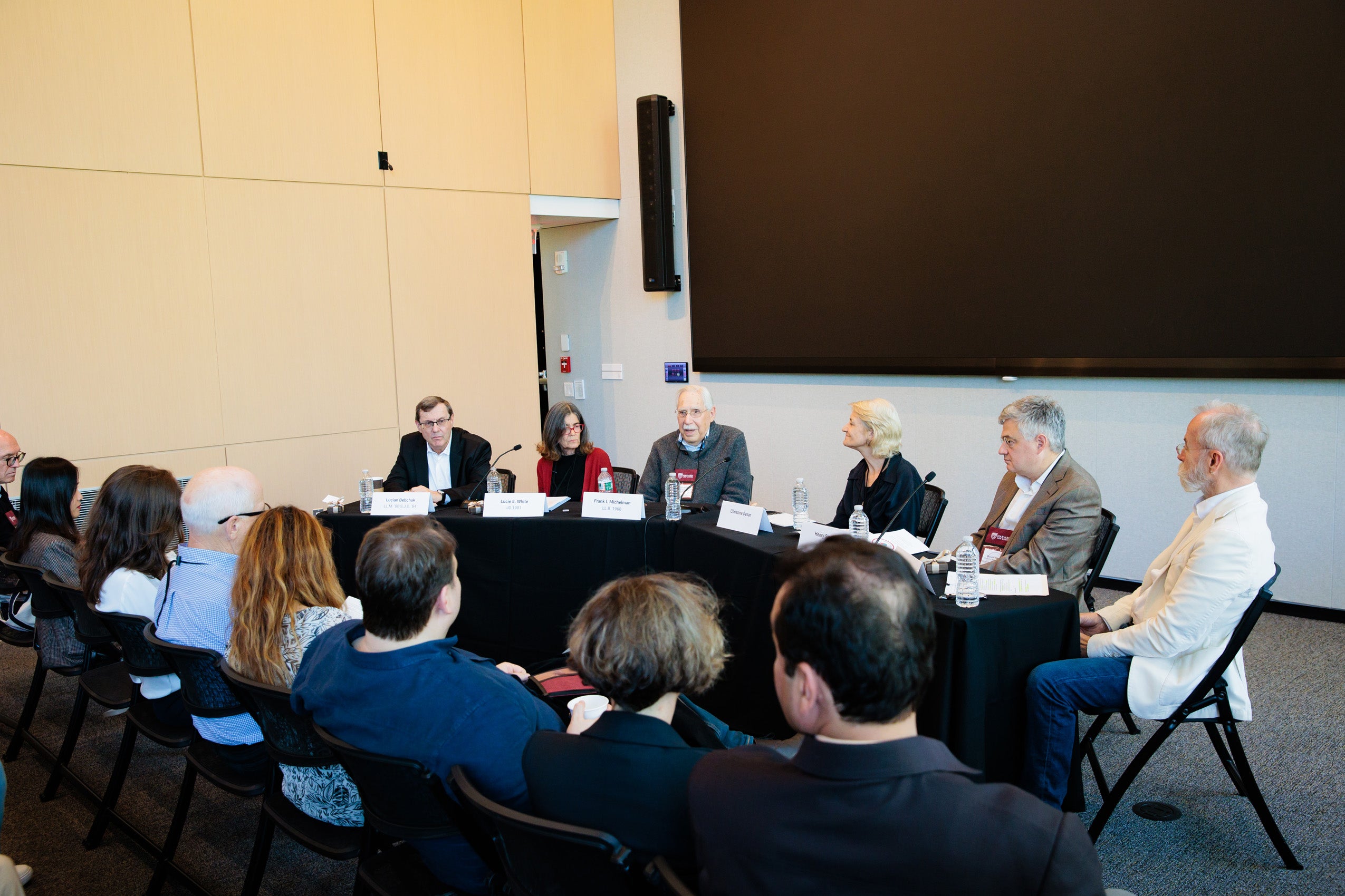 A panel of six speaks in front of an audience in a room