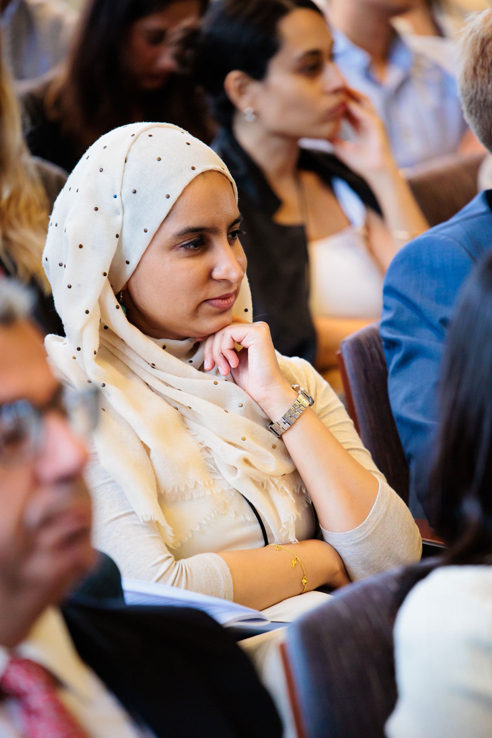 A close up of a woman sitting in a crowd listening to a speaker