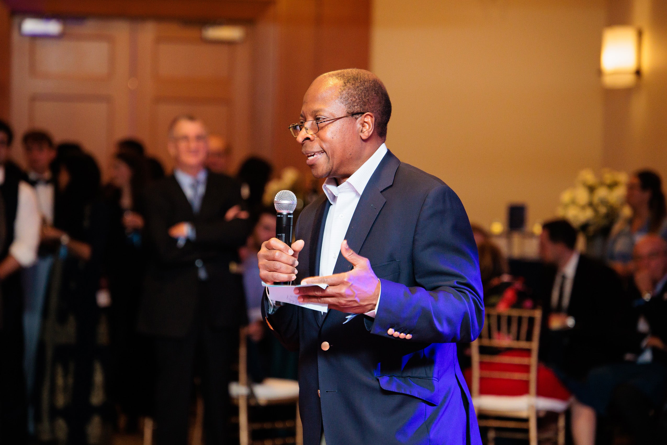 A man with a microphone speaks to a crowd in a room.