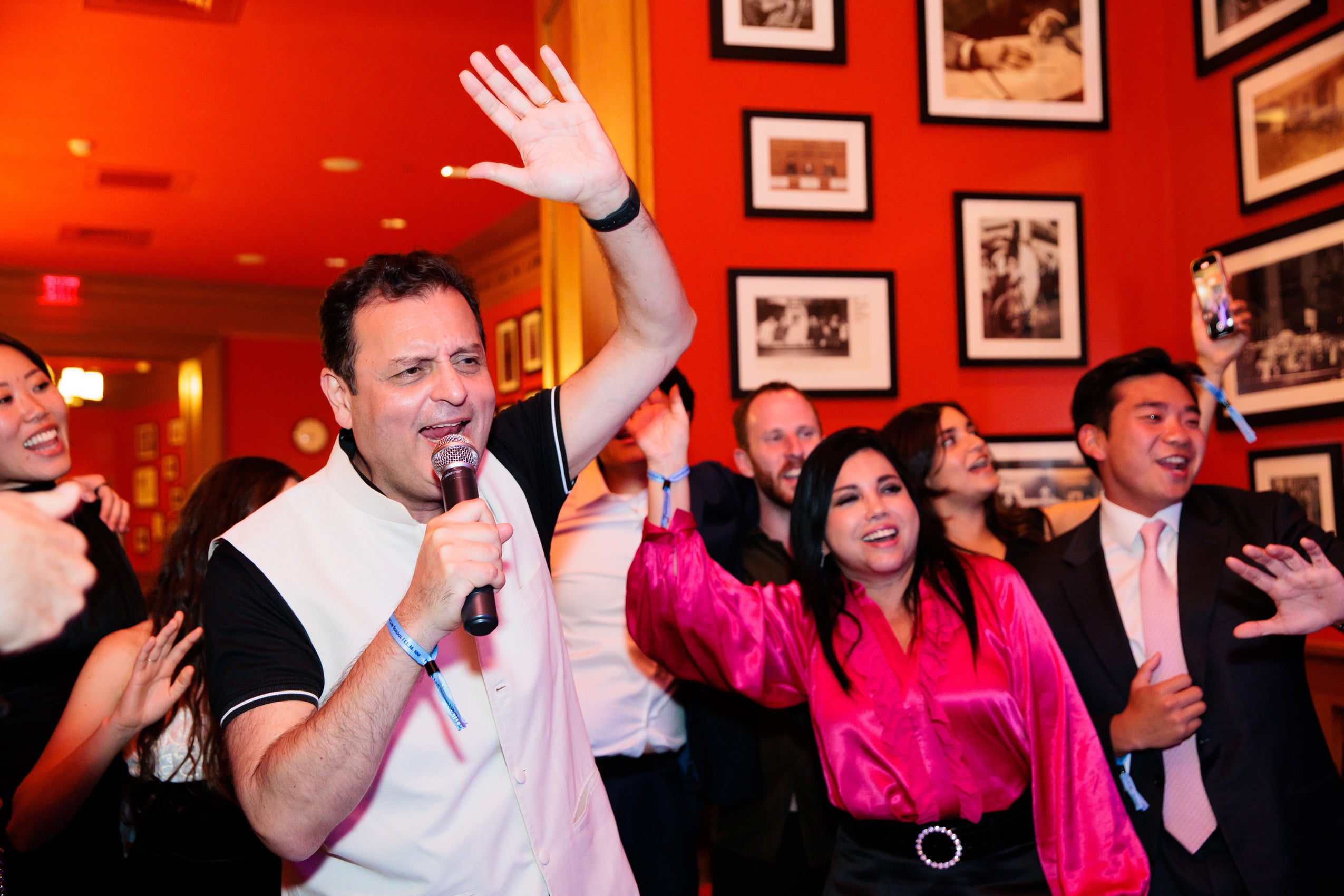 A man holding a microphone sings with a group of others at a party.