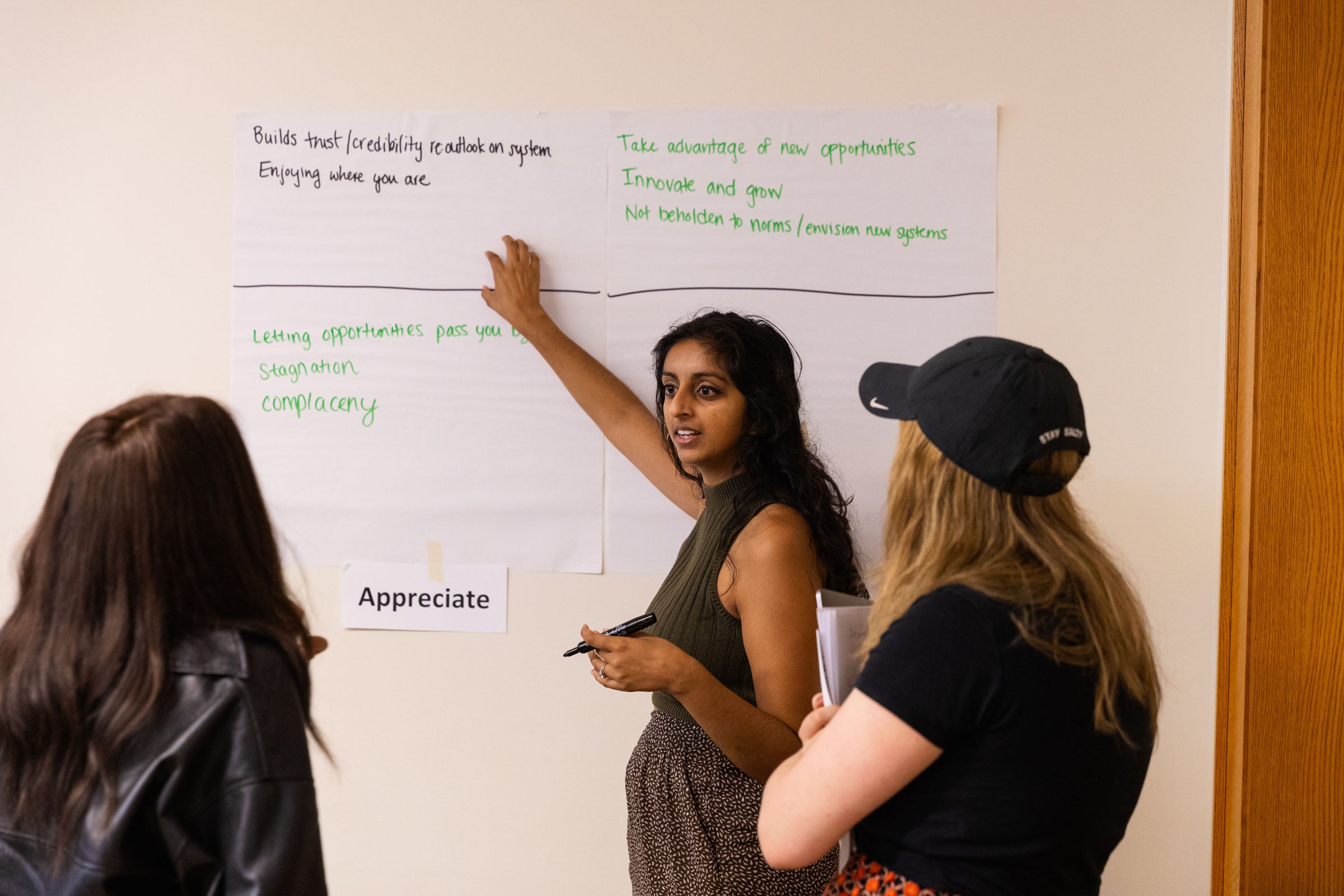 A person writes on a white board in front of a room