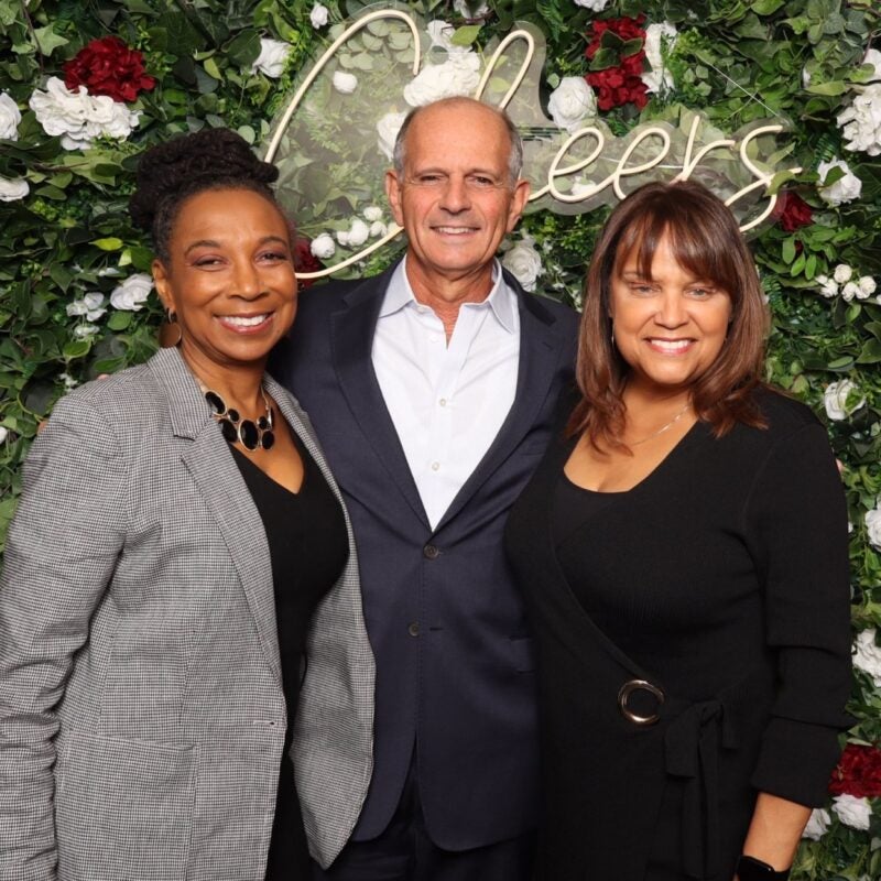 Alumni posing for a photo in front of a sign that says 