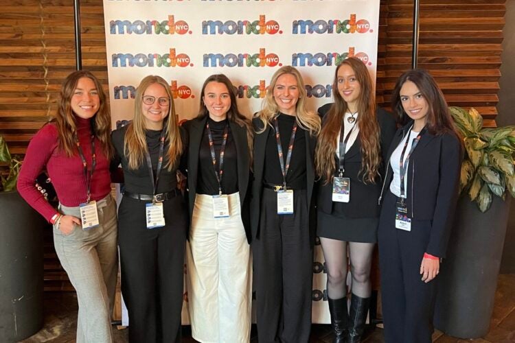 Six RAP students stand in front of a Mondo conference banner