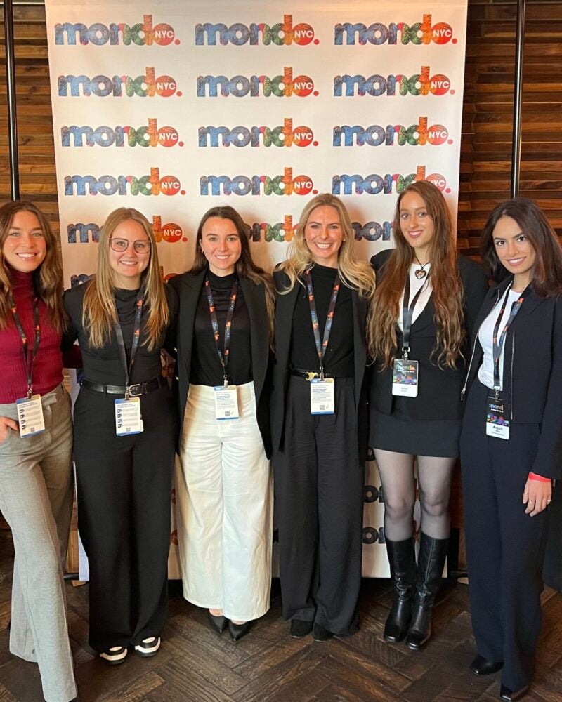 Six RAP students stand in front of a Mondo conference banner