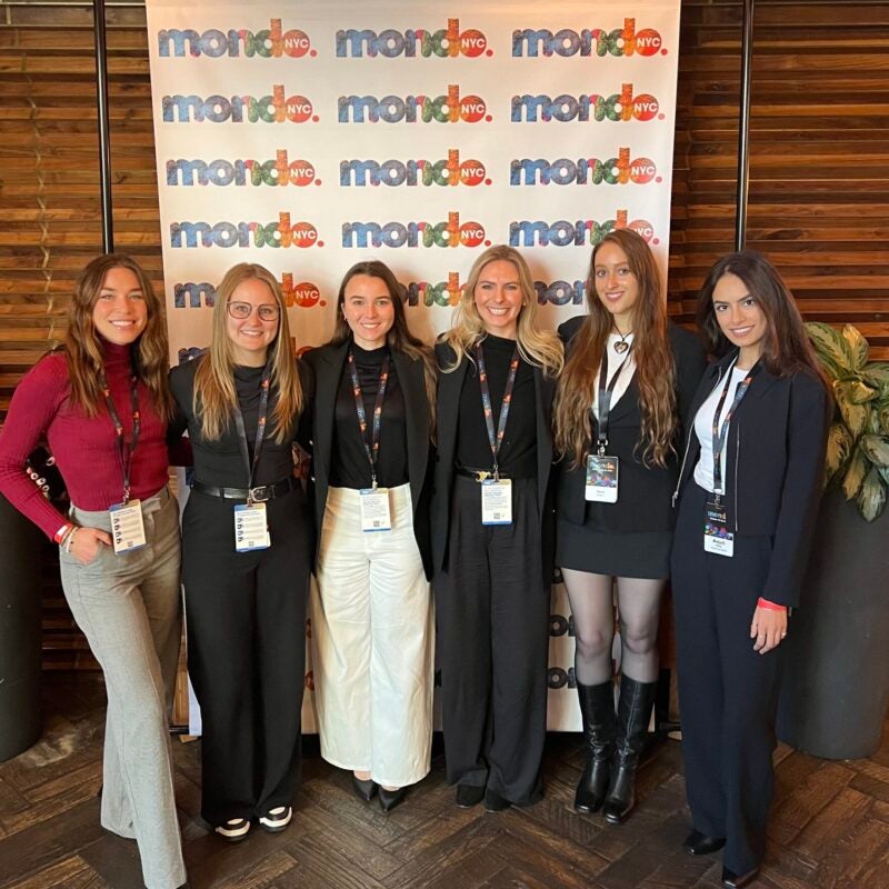 Six RAP students stand in front of a Mondo conference banner