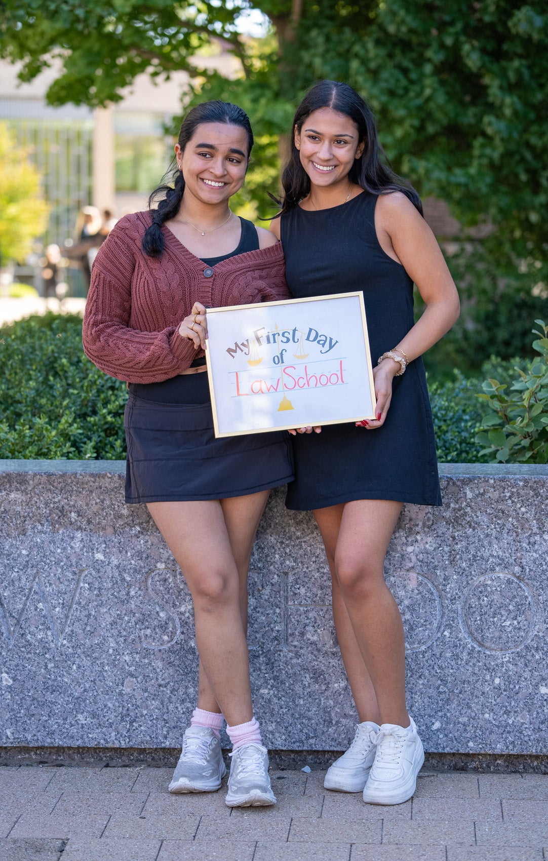 Two students pose in front of a granite Harvard Law School sign holding a framed sign that says 