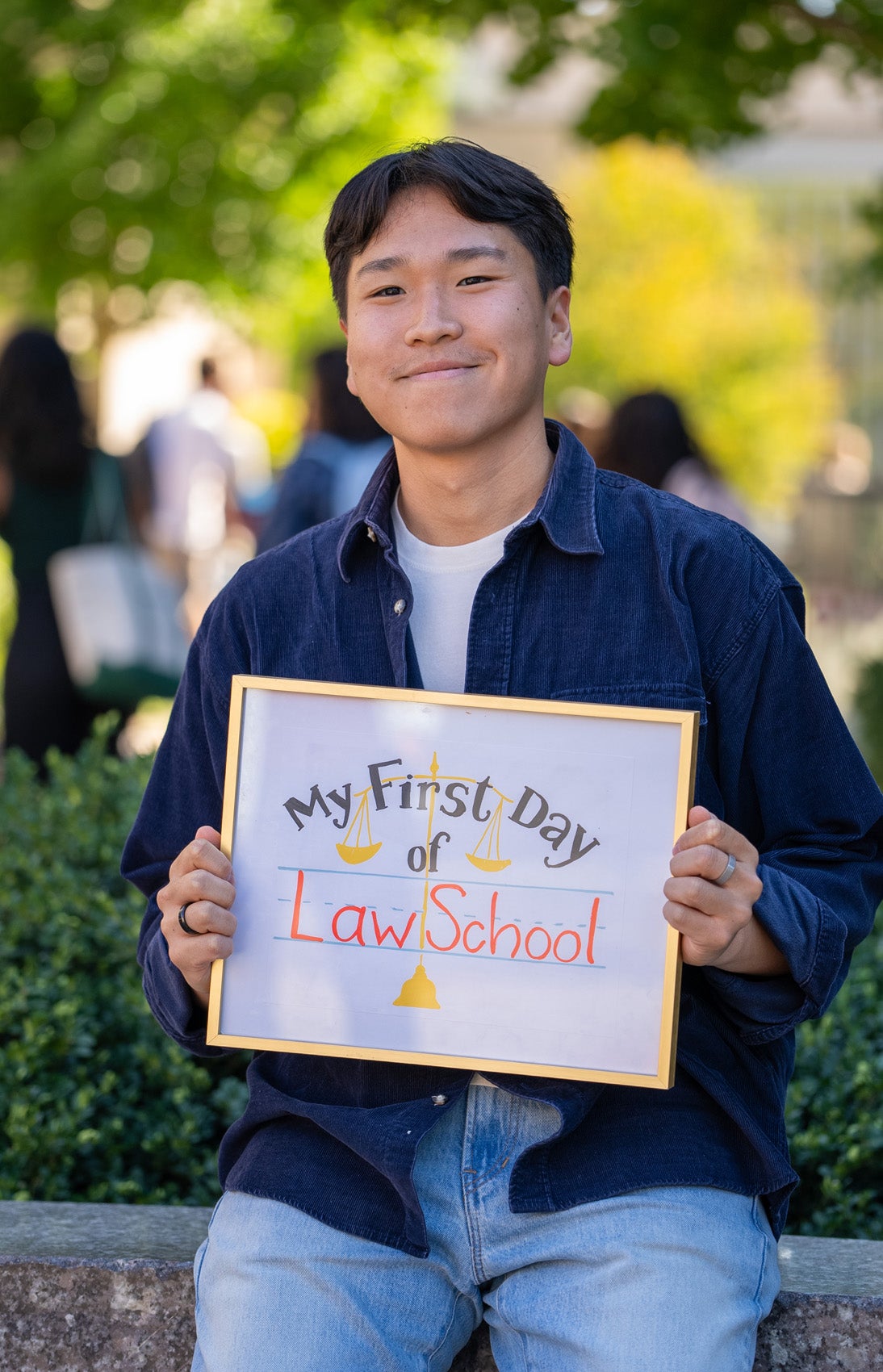 Two students pose in front of a granite Harvard Law School sign holding a framed sign that says 