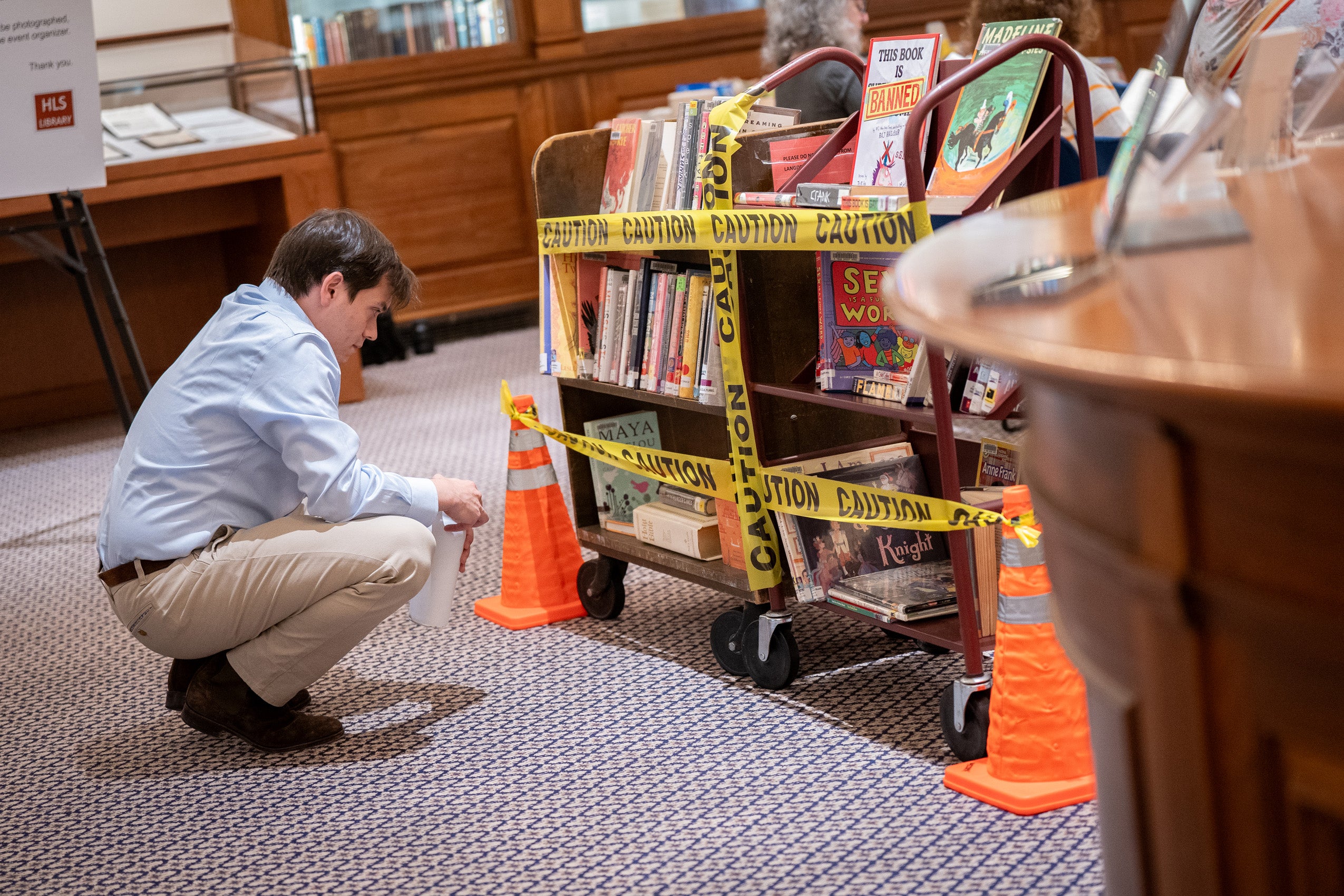 An individual looks at a rack of books with caution tapes across it in a library.
