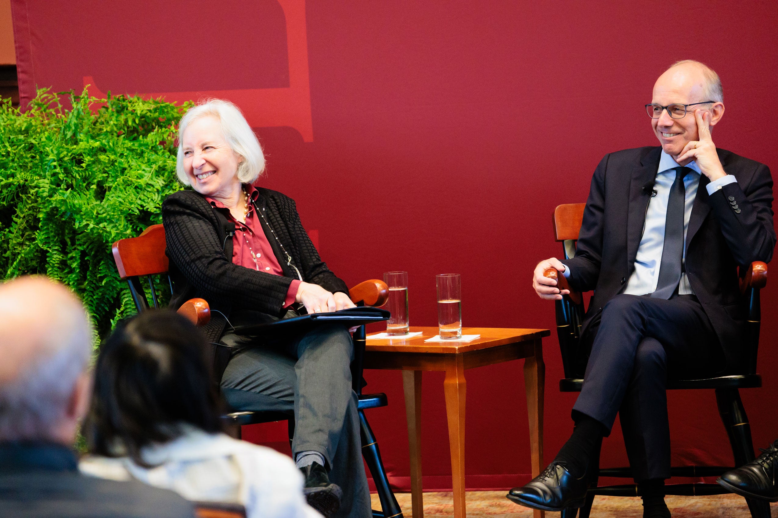 Two people sitting on chairs on a stage speaking