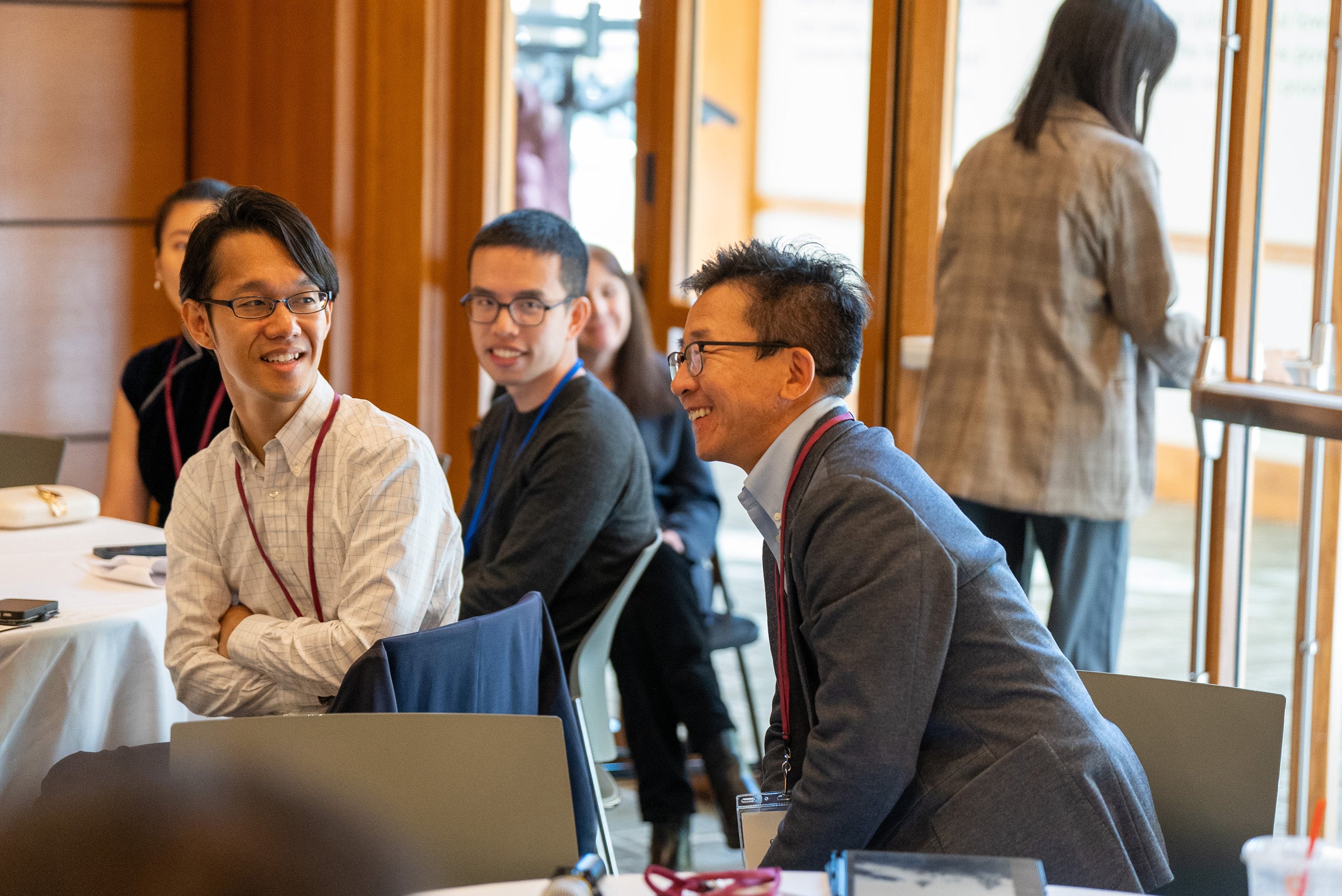 A person sitting at a table in a room filled with other tables smiles in response to a remark