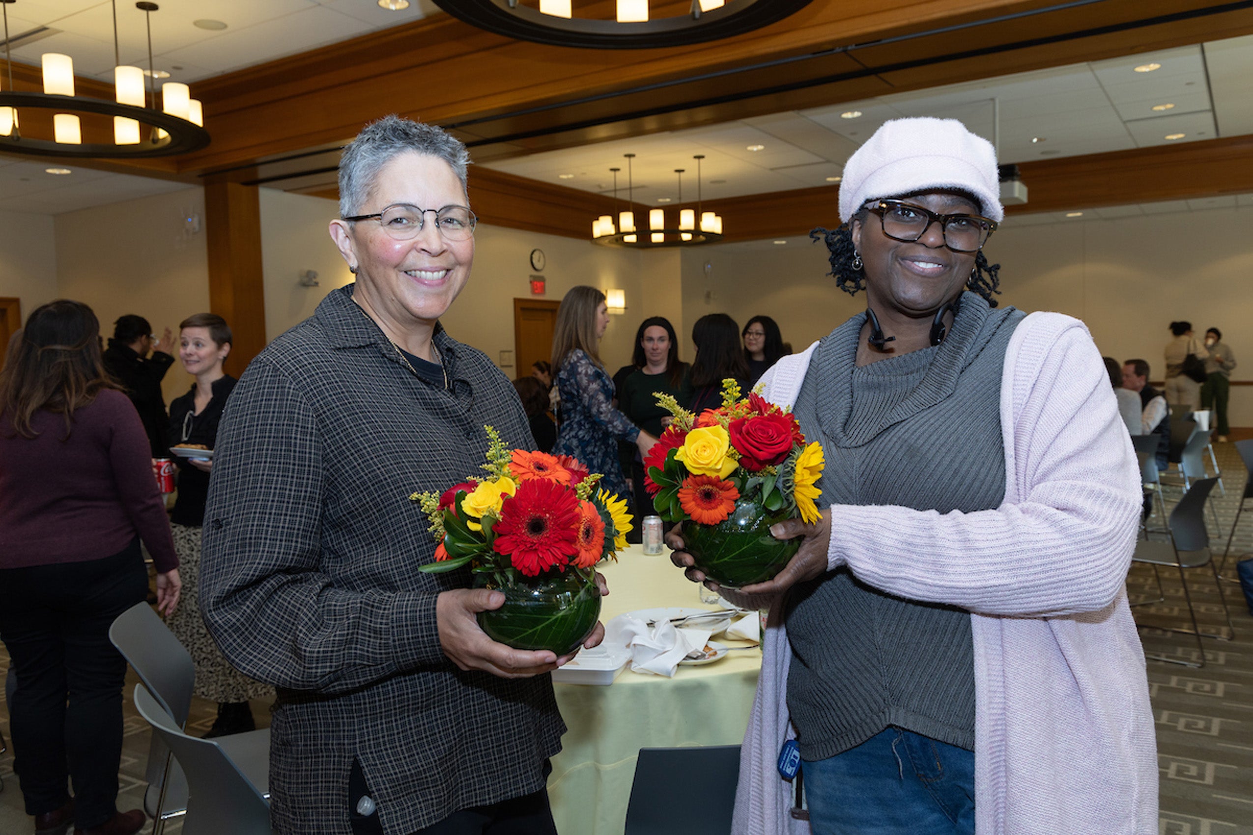 Two women holding a colorful flower arrangements at an event pose for the camera.
