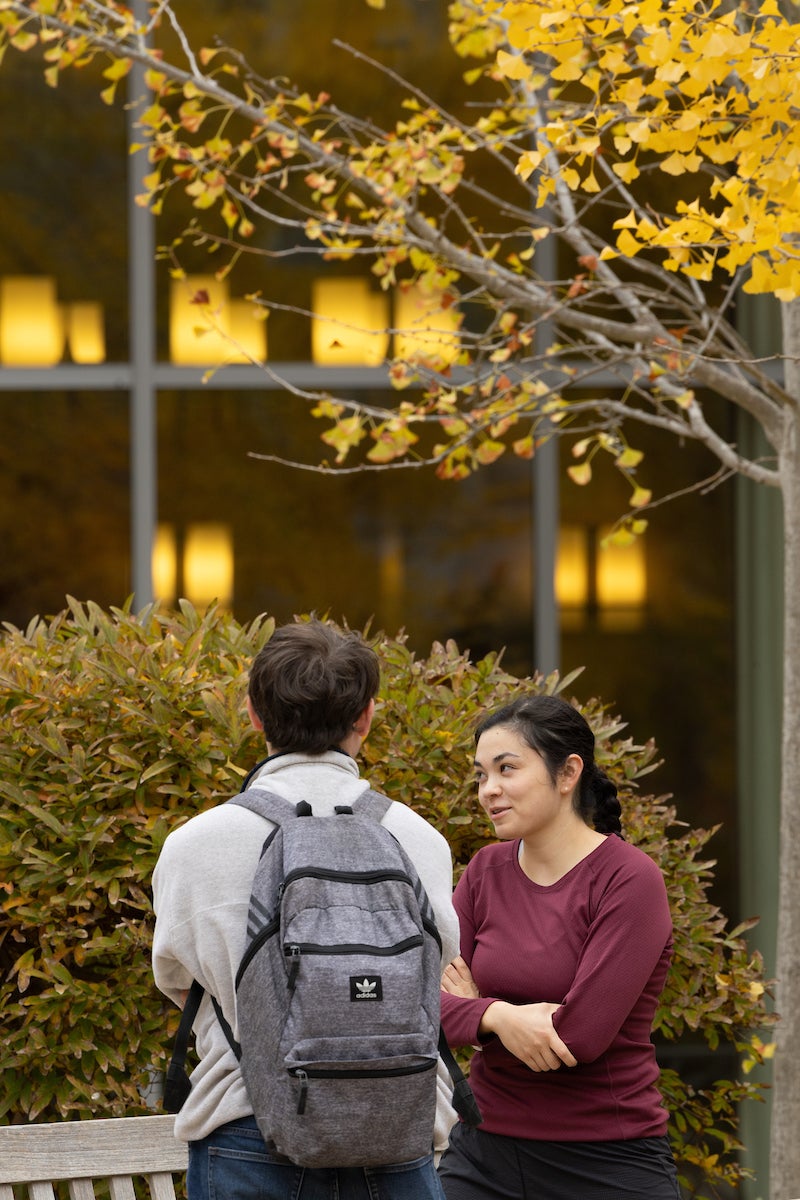 Two people chat outside on campus in the fall.