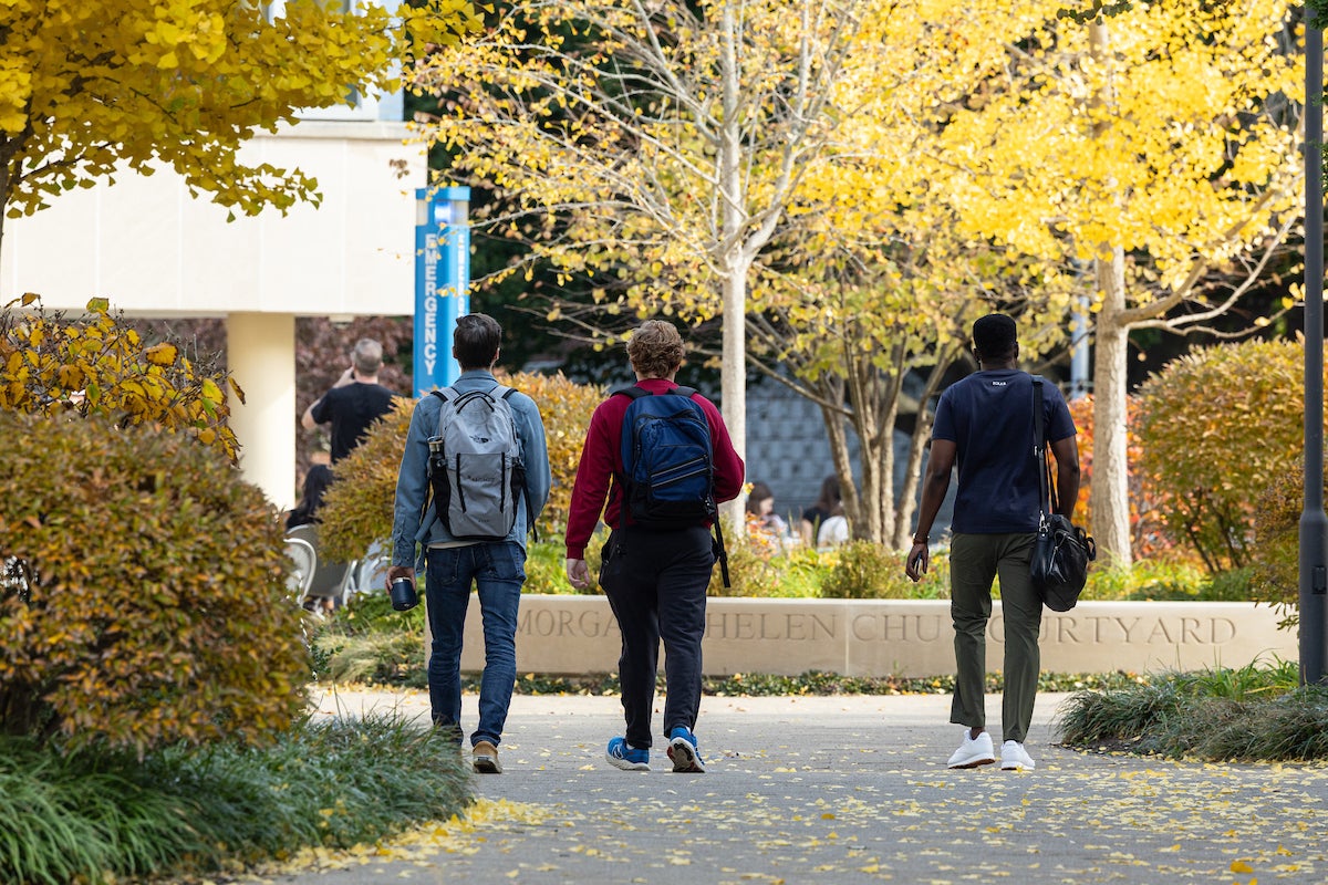 Three students walk through campus in the fall.