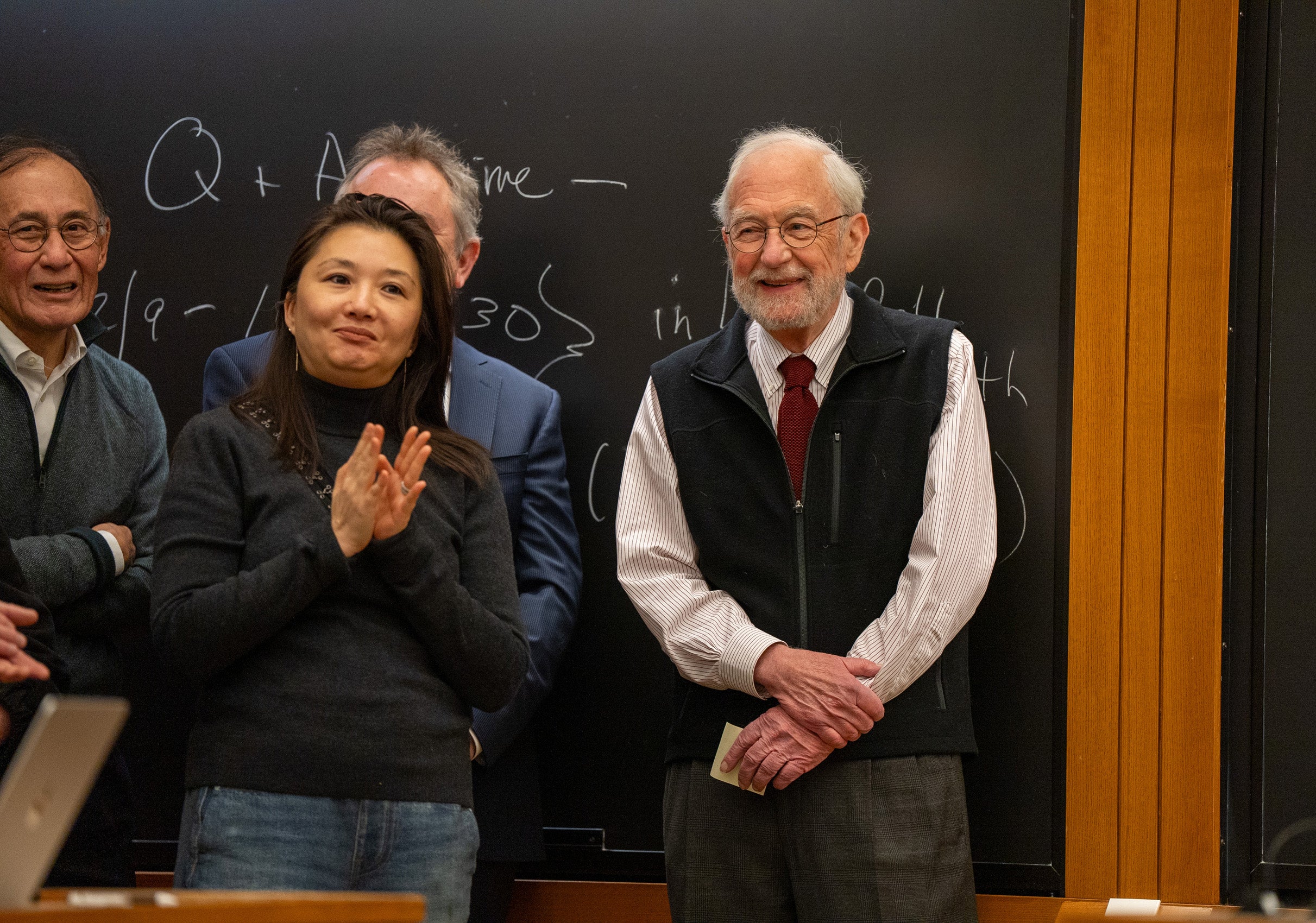 A man stands in the front of a classroom with several colleagues nearby