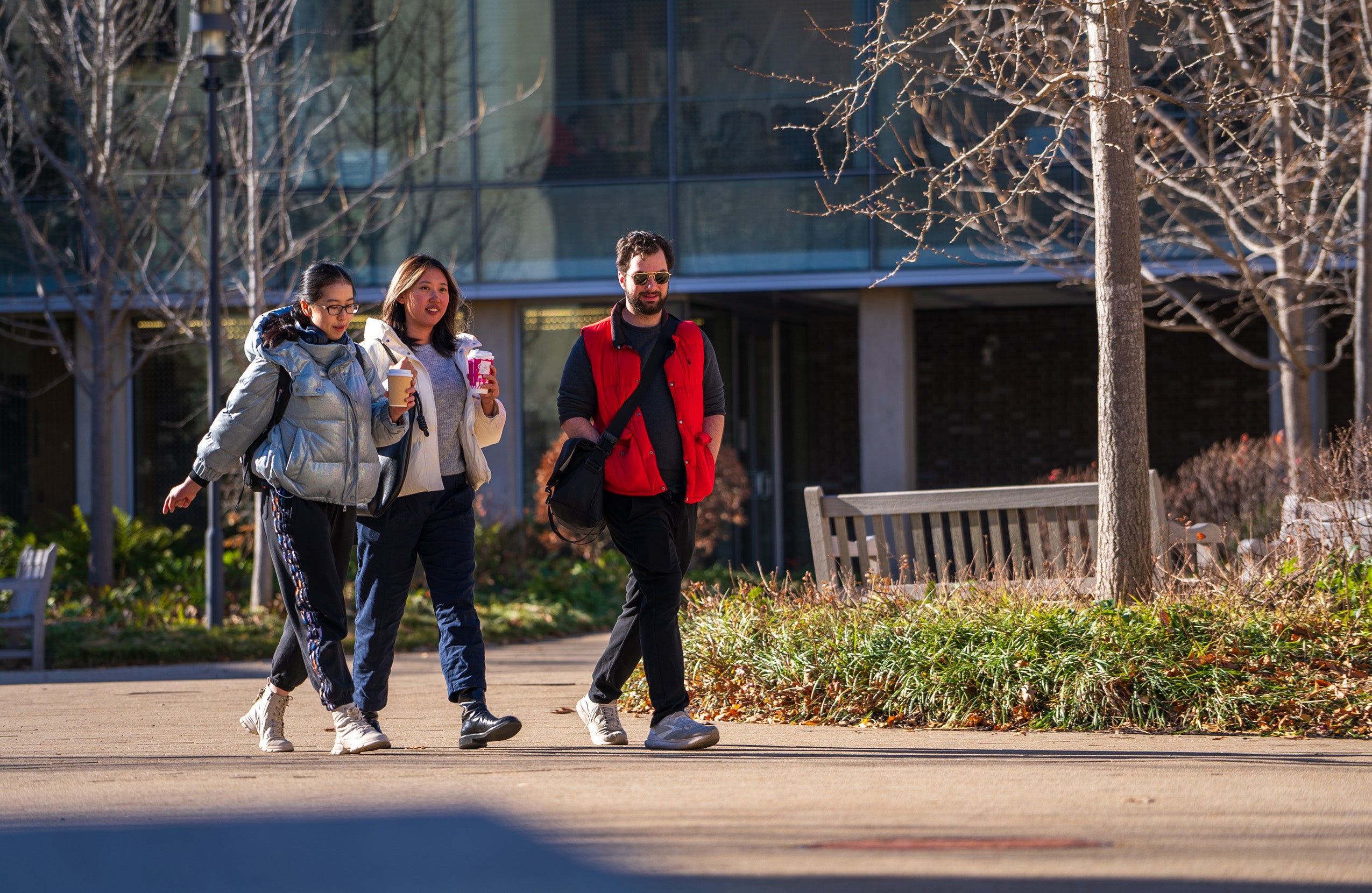 Three students bundled in winter jackets walk across campus