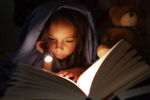 Girl reading book with flashlight.