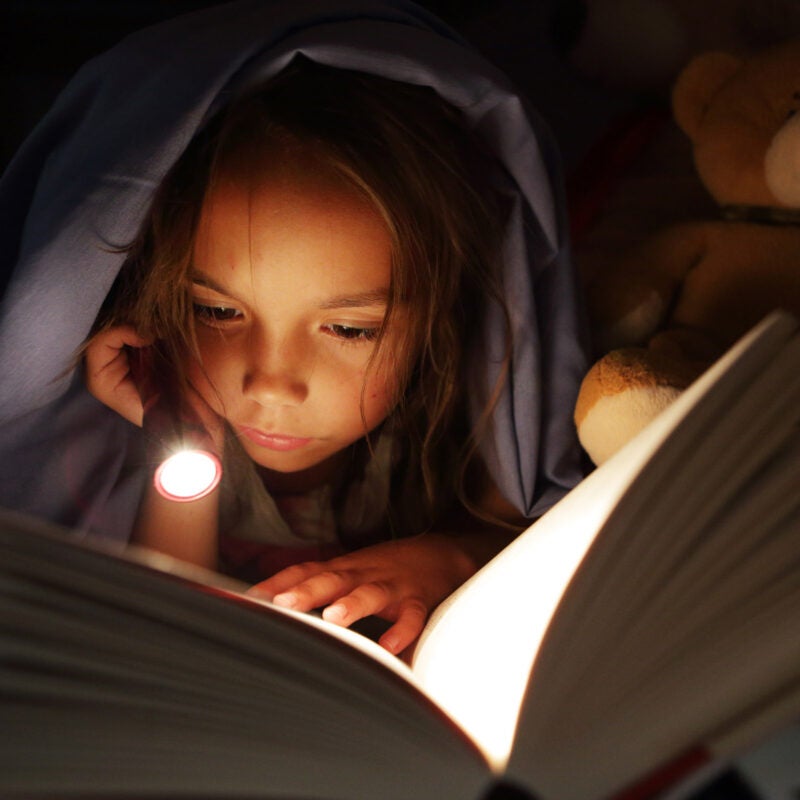 Girl reading book with flashlight.