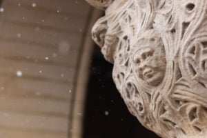 A detail of a carved face figure with a pleasant expression at the top of a stone column on a snowy day.