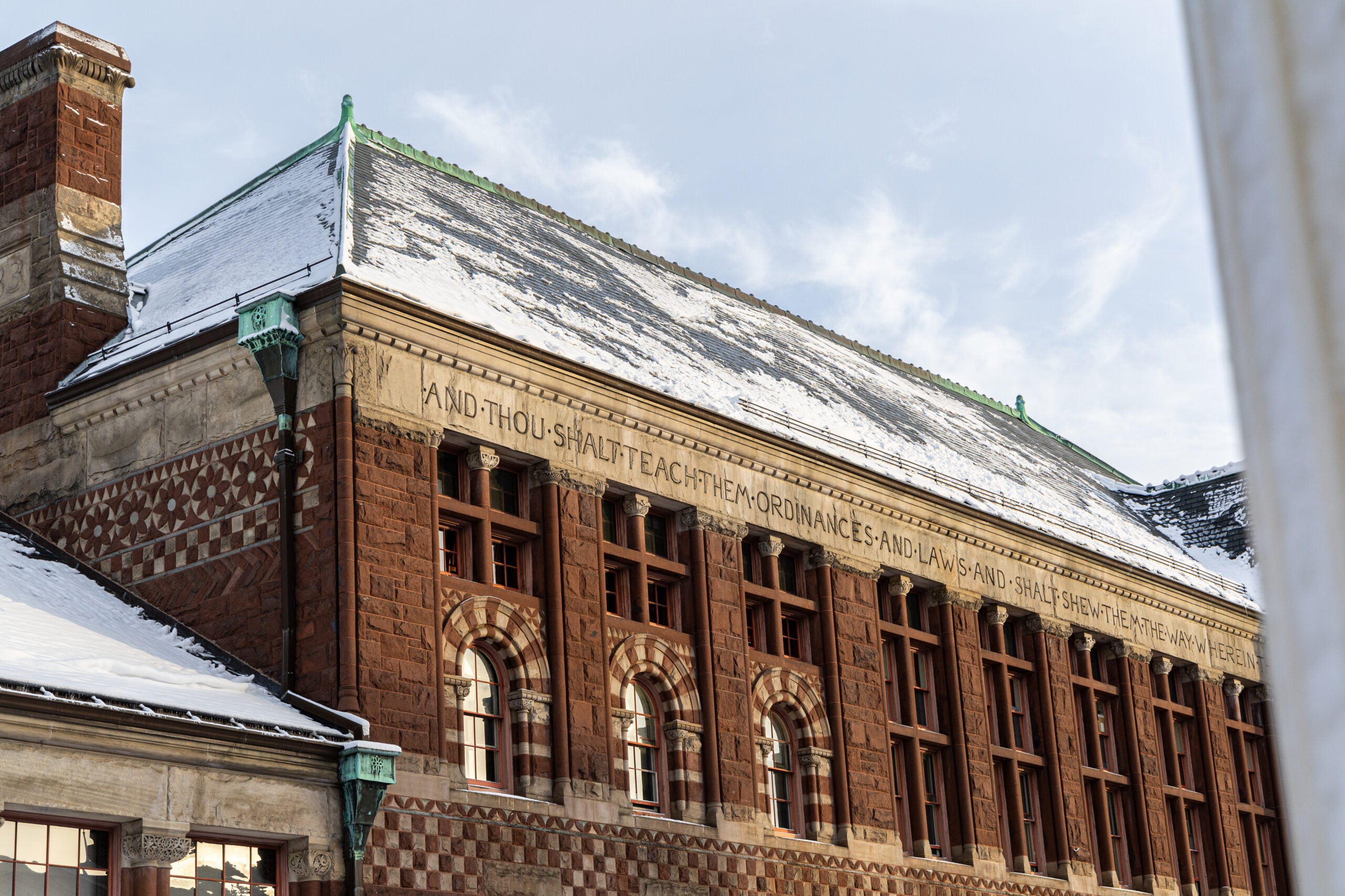 A wide view of the second story of a lightly snow-covered red-brick building as a hint of sunshine peaks through.