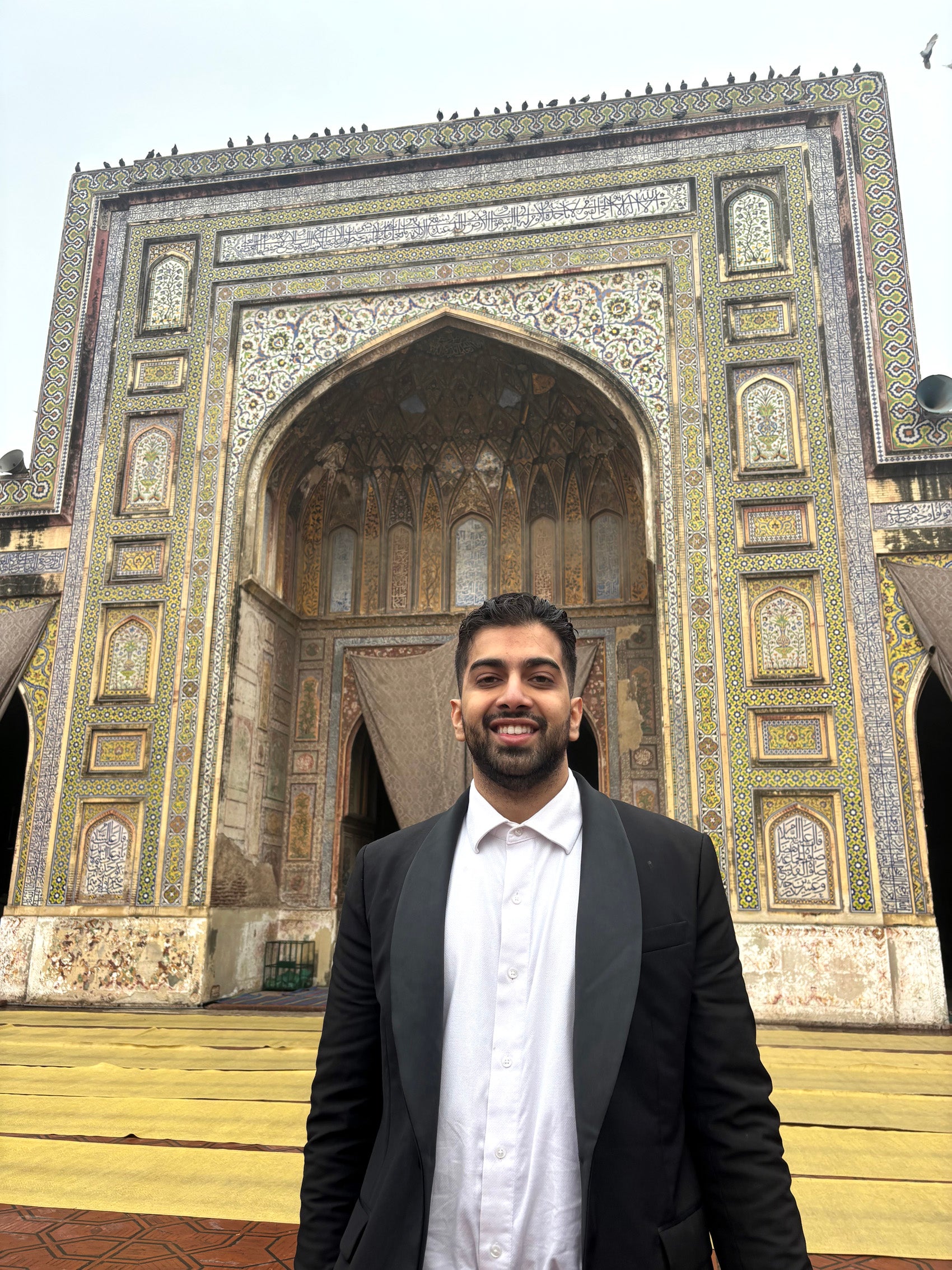 A man stand in front of an arch covered in mosaic designs.