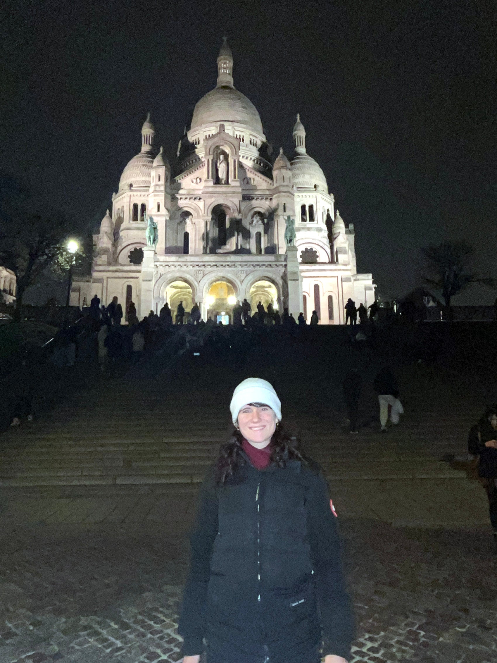 A woman stands in front of the Sacre Coeur at night.