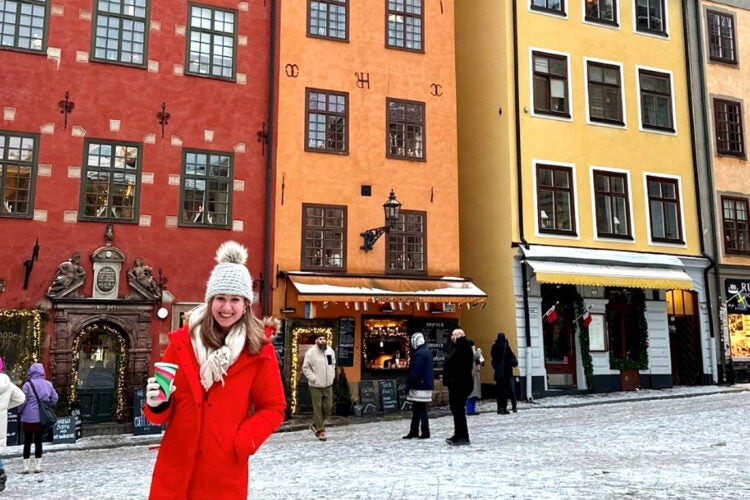 A woman stands on a road in front of three brightly colored buidlings