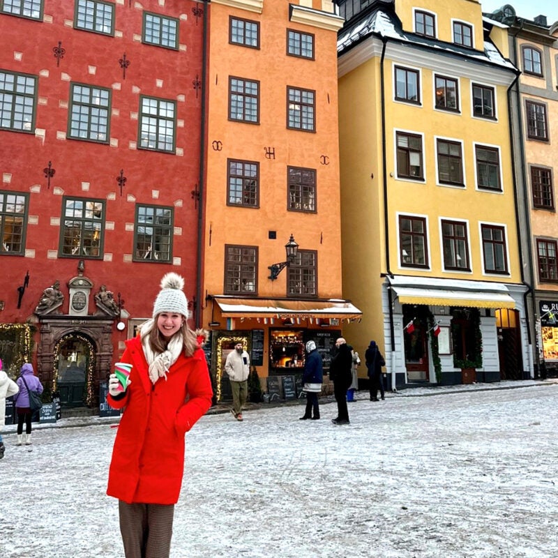 A woman stands on a road in front of three brightly colored buidlings