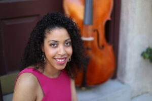 Krysta Hyppolite smiles next to a cello