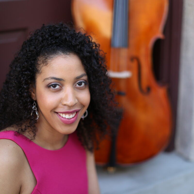Krysta Hyppolite smiles next to a cello