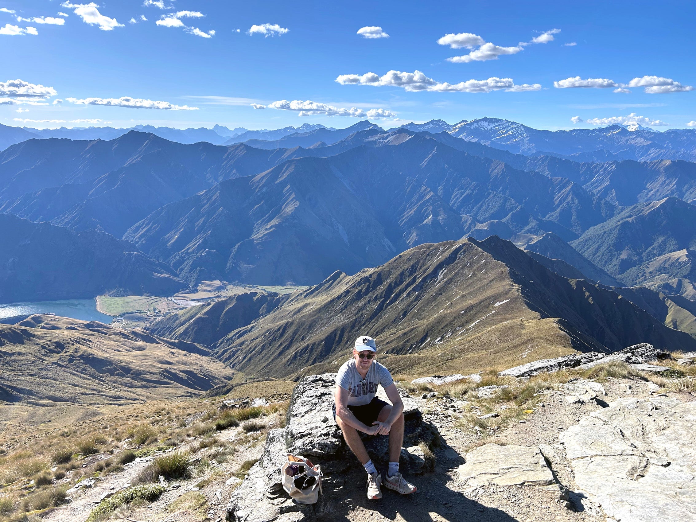 A man sits on a rock, a mountain range in the background.