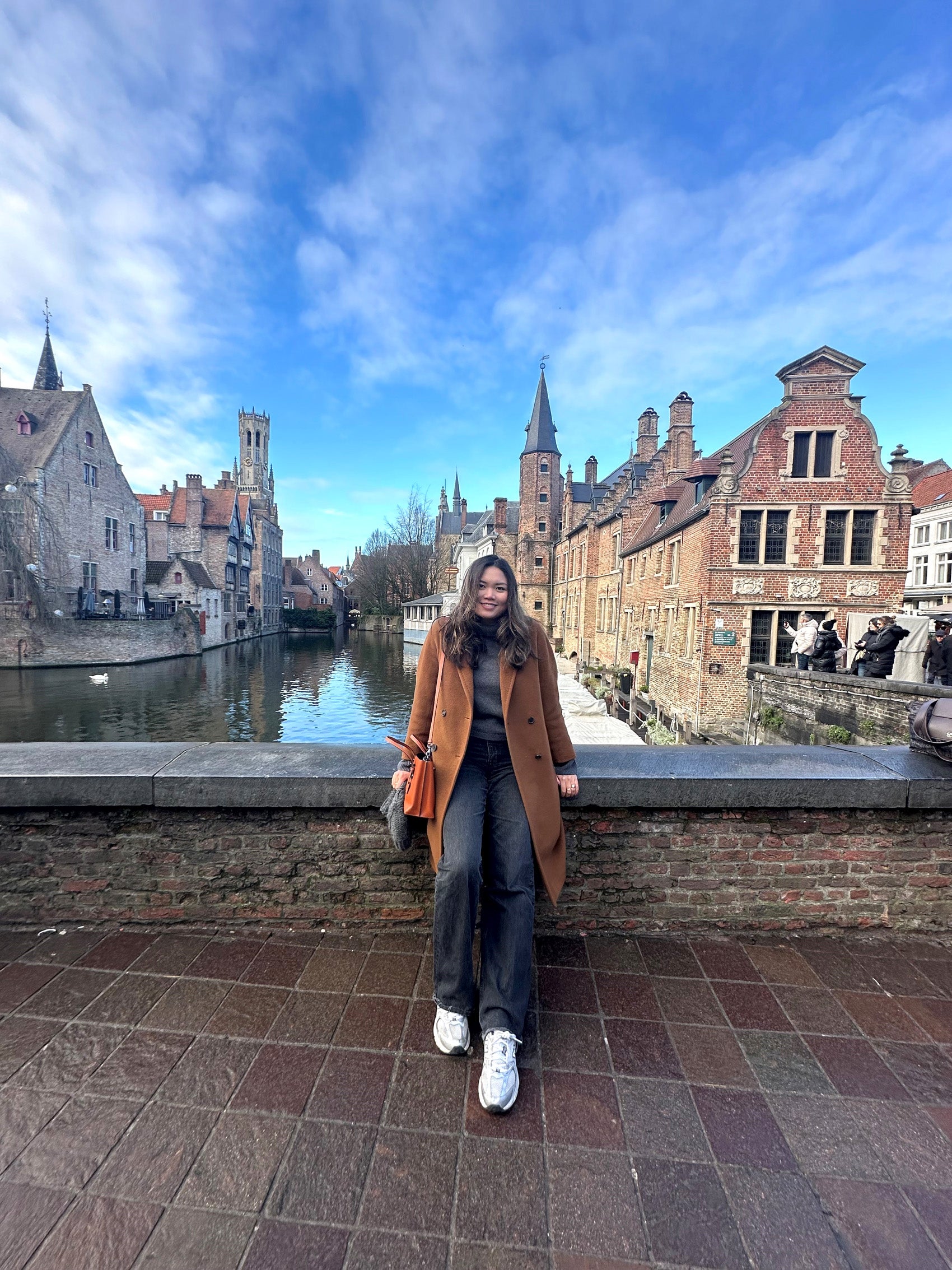 A woman leans against a brick railing near a waterway with buildings on both sides.