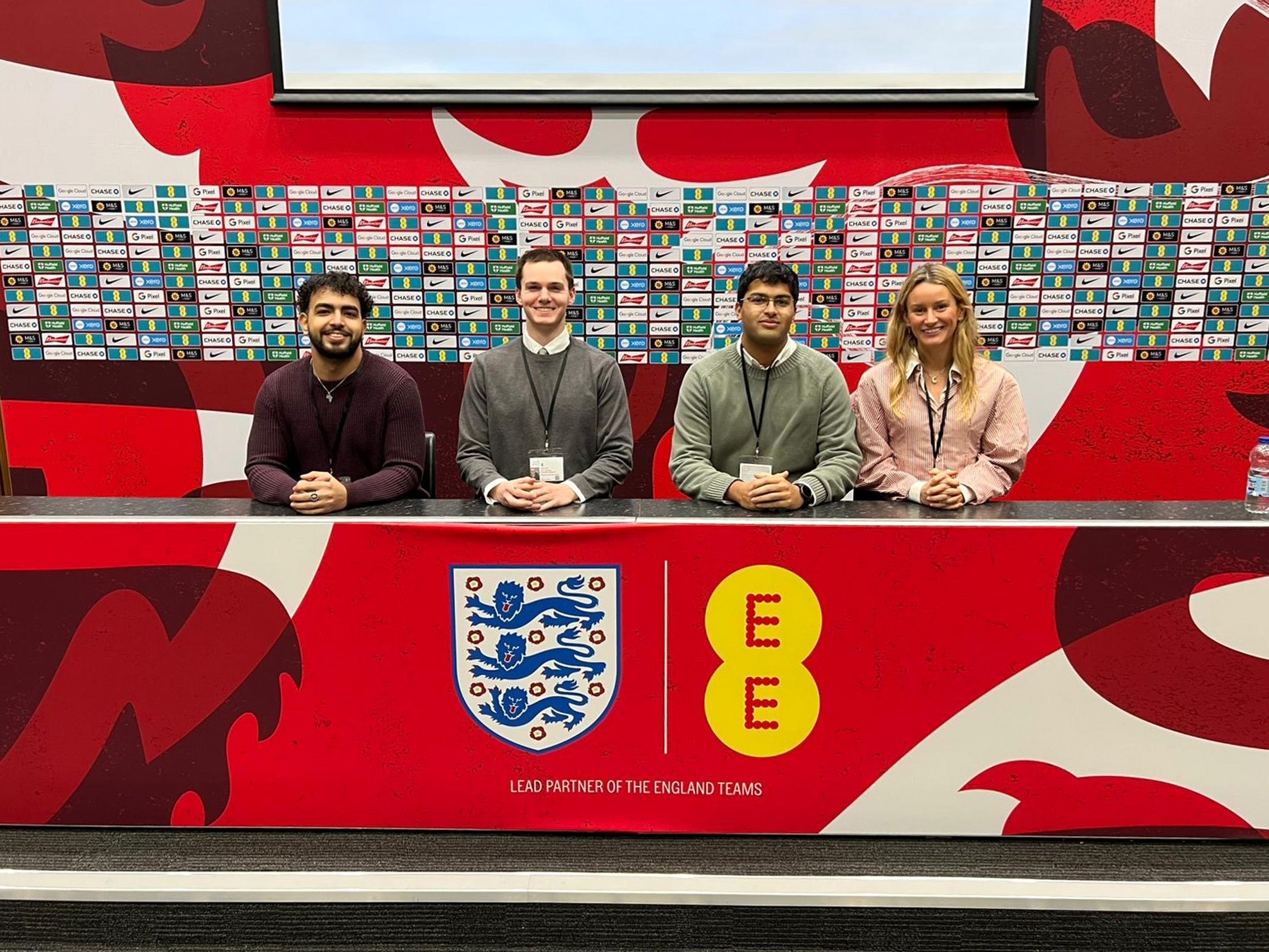 Four people sit behind a brightly colored long desk.