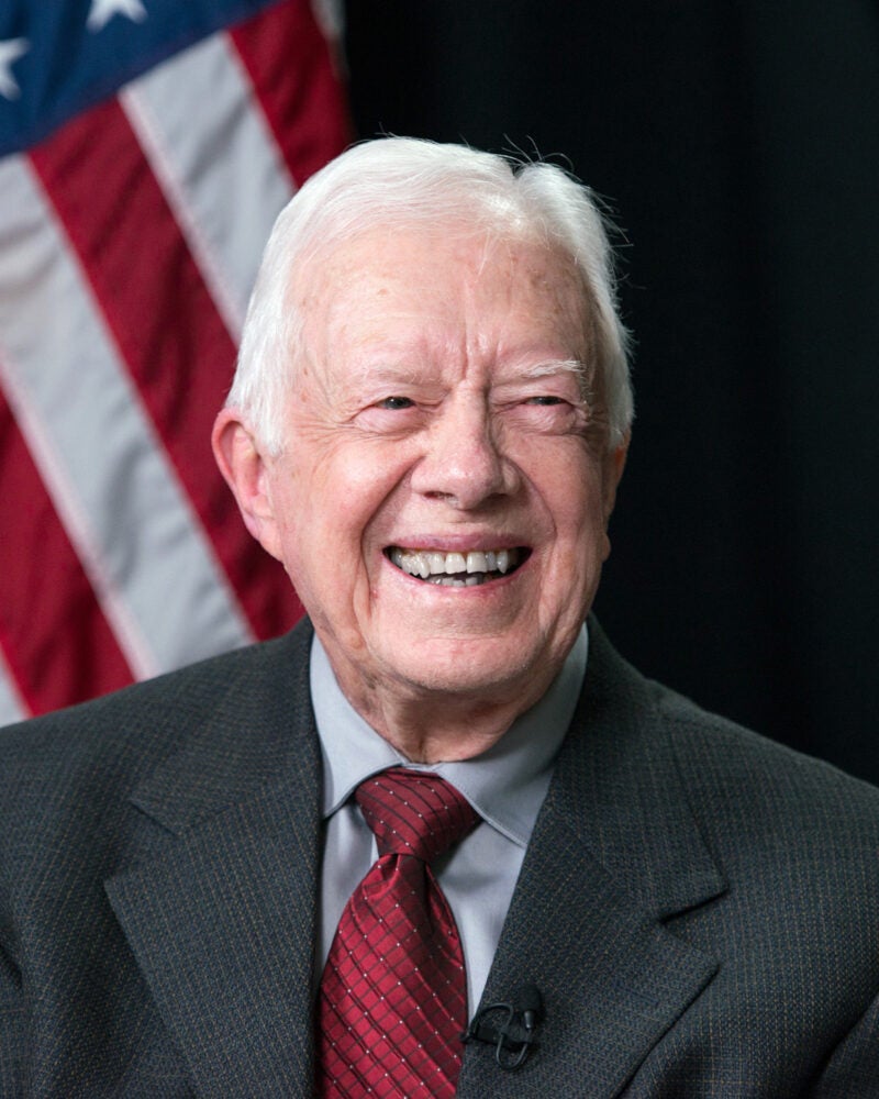 President Jimmy Carter smiles with American flag behind him.