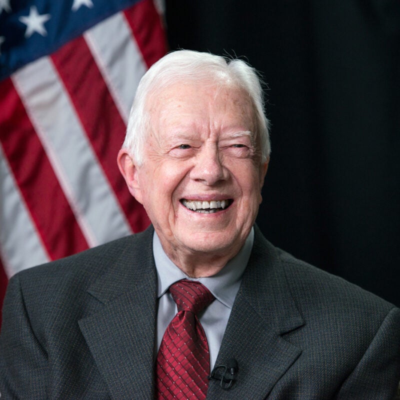 President Jimmy Carter smiles with American flag behind him.