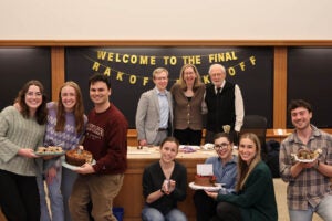 Three small groups of students holding a baked good and a group of judges pose in front of the sign 