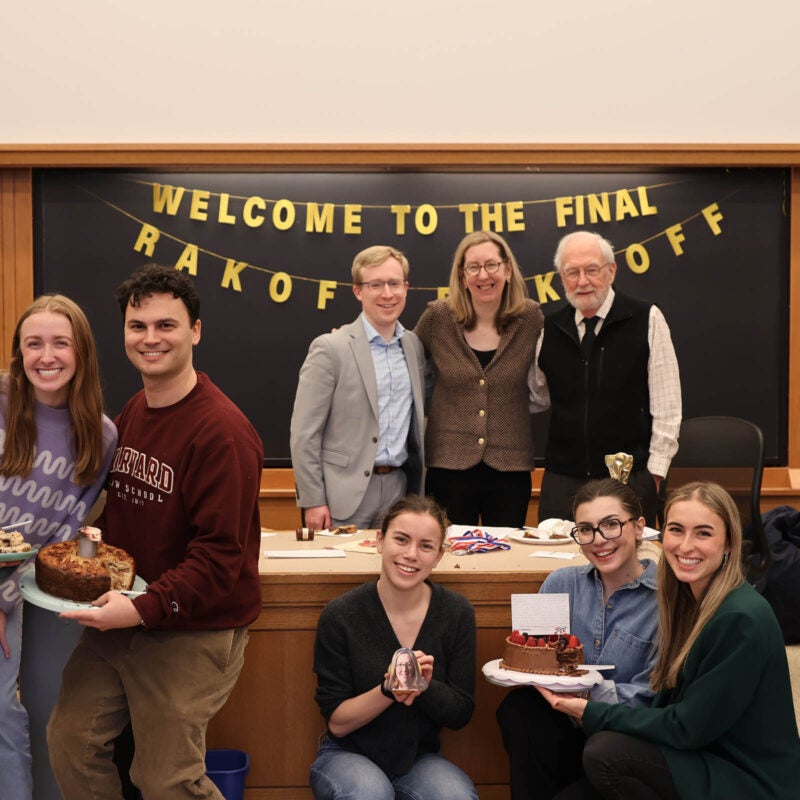 Three small groups of students holding a baked good and a group of judges pose in front of the sign 
