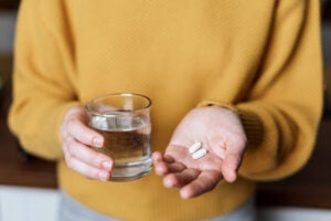 Person holding two pills and a glass of water.