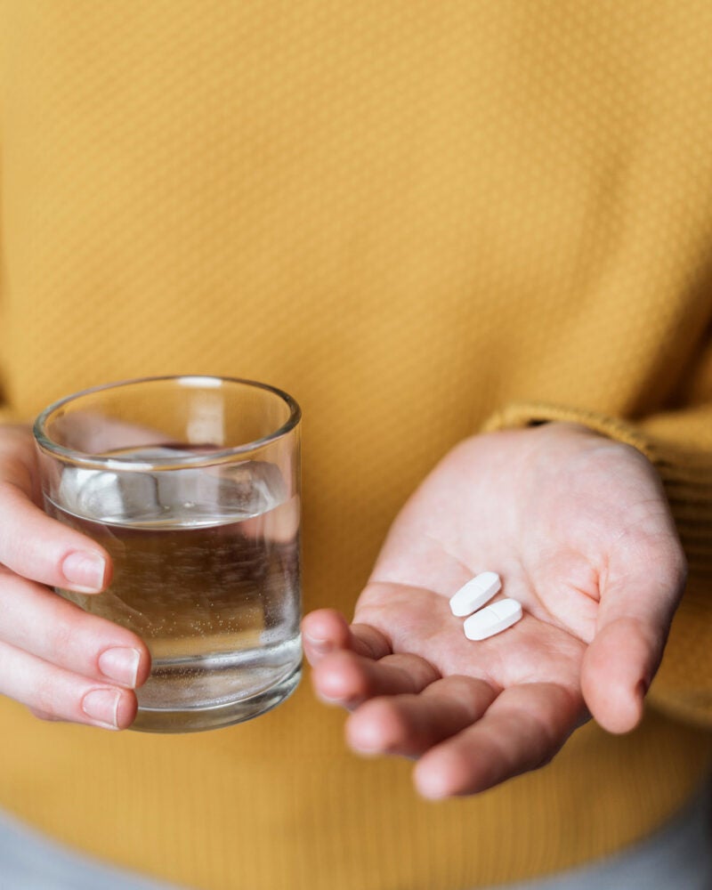 Person holding two pills and a glass of water.