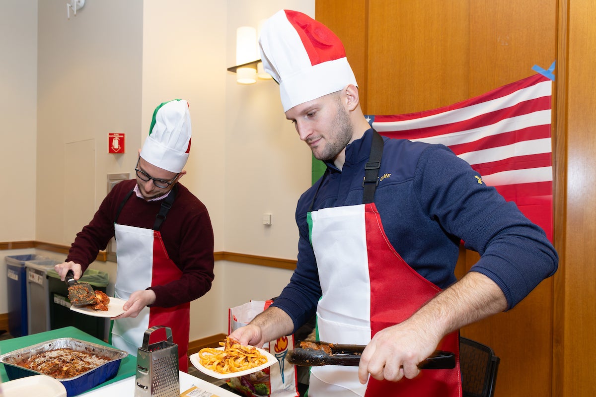 Two students wearing chef's hats serve food.