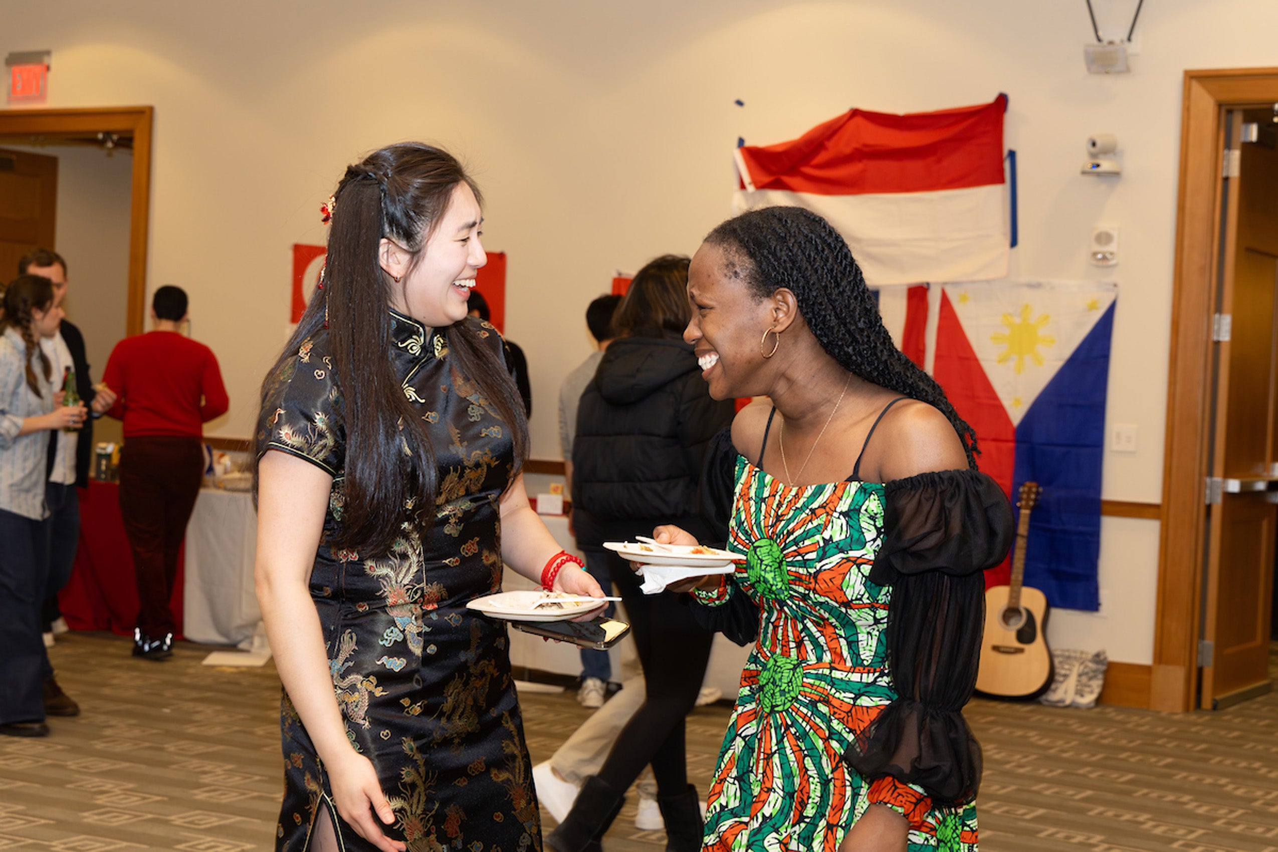 Two students holding plates of food enjoy a light moment at an event.