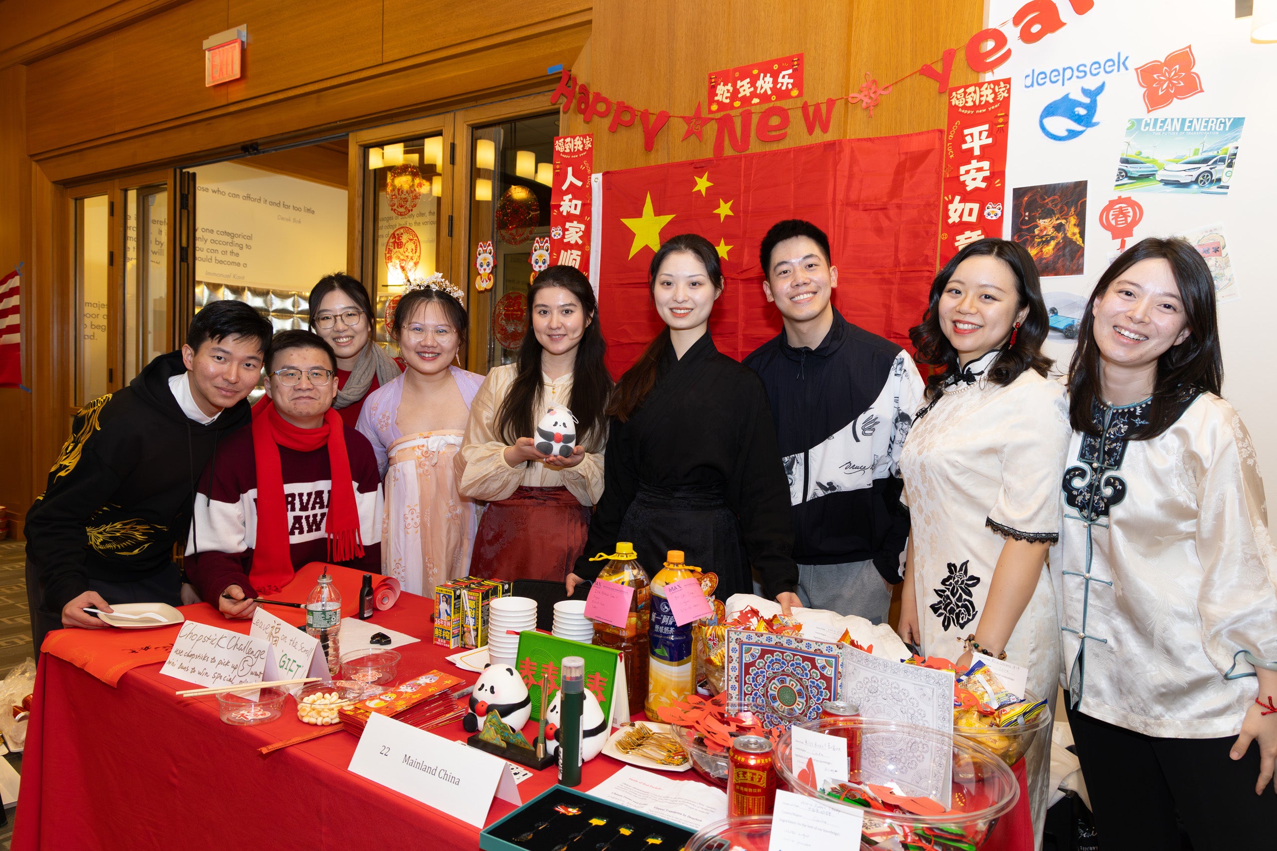 Nine students pose for a photo in fornt of a flag from their country and a display of food and other items.