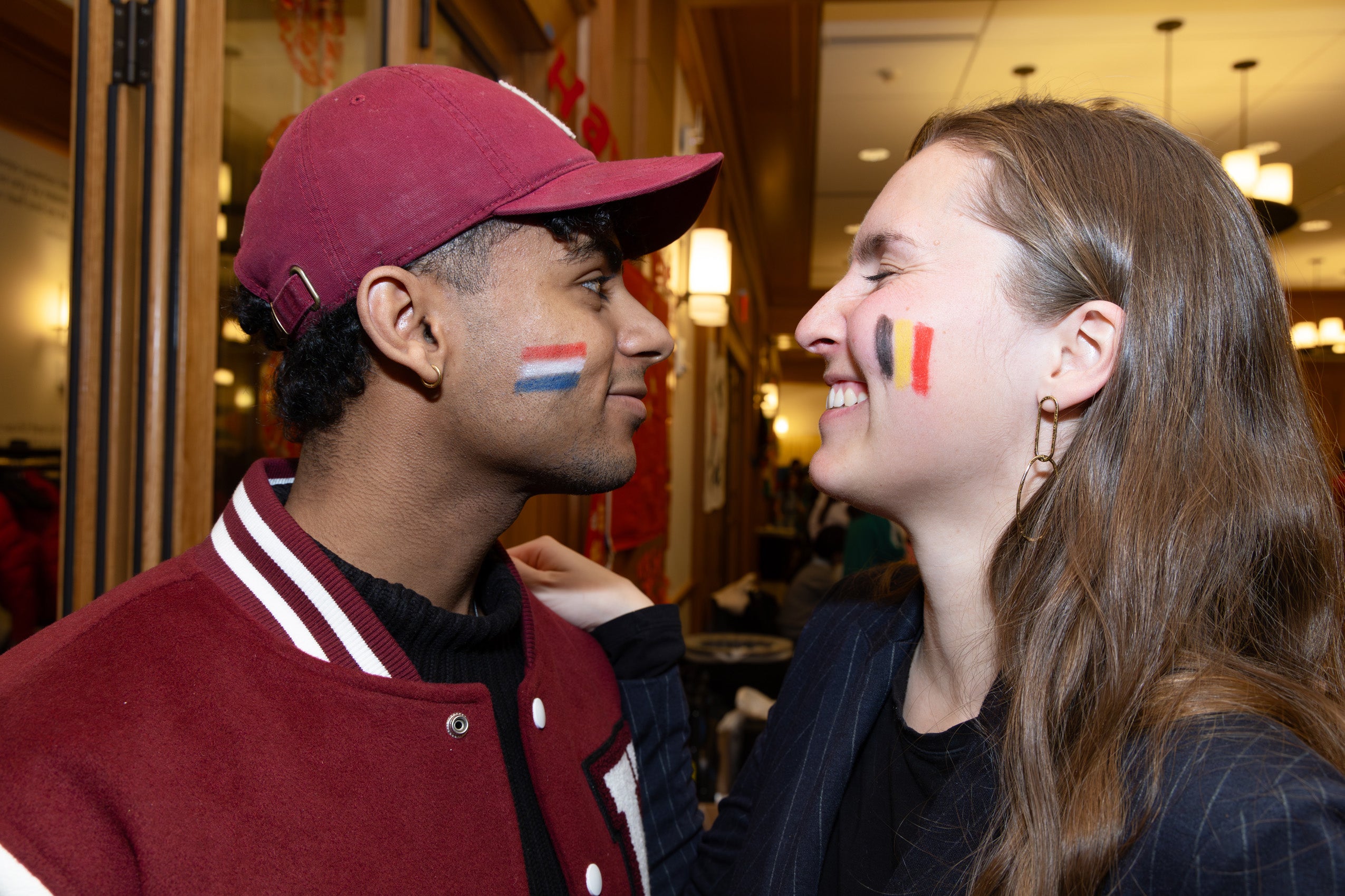 Two students turn towards each other displaying flags painted on their cheeks.