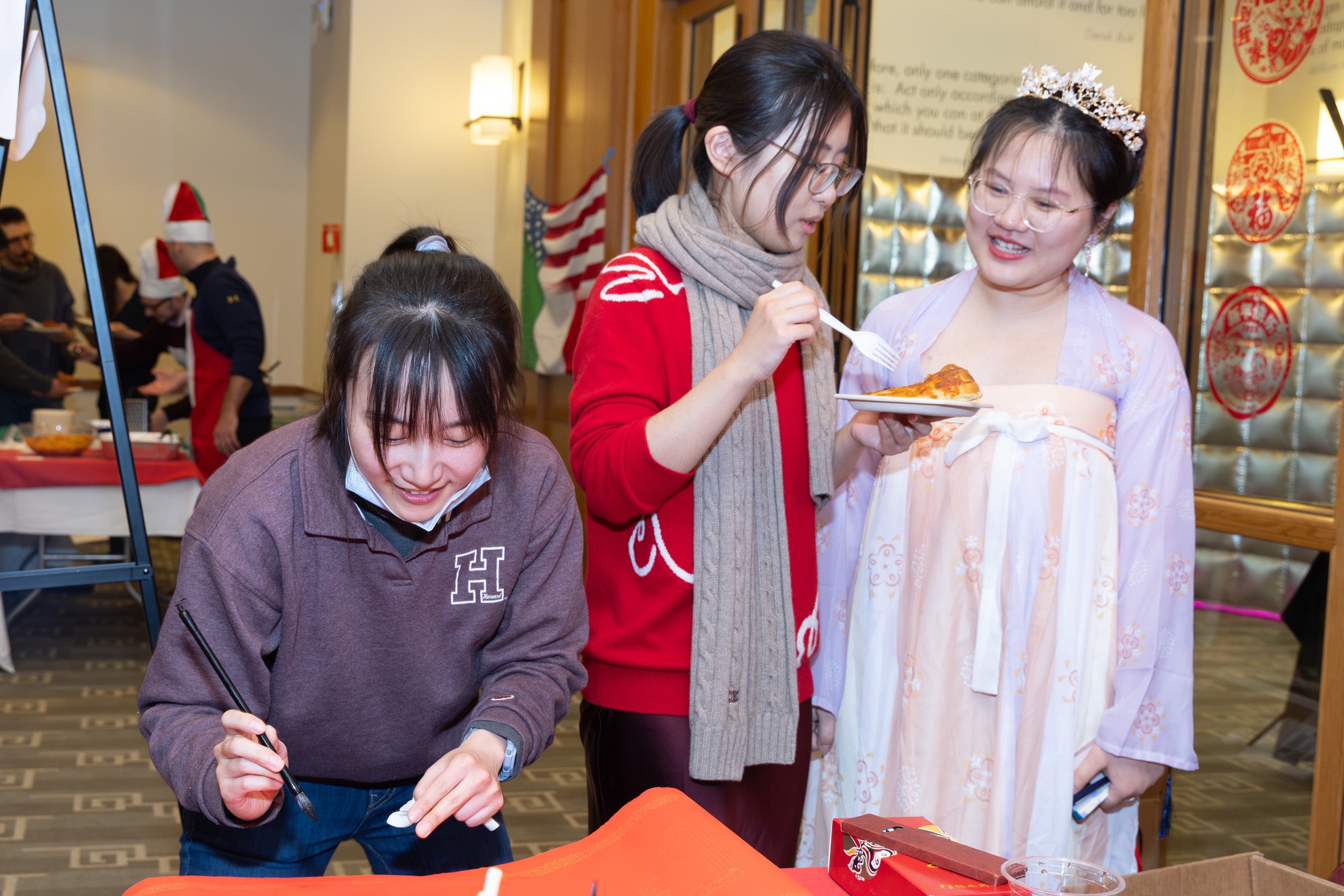 Three students--one wearing traditional dress at an event--sample food, and work on a display.