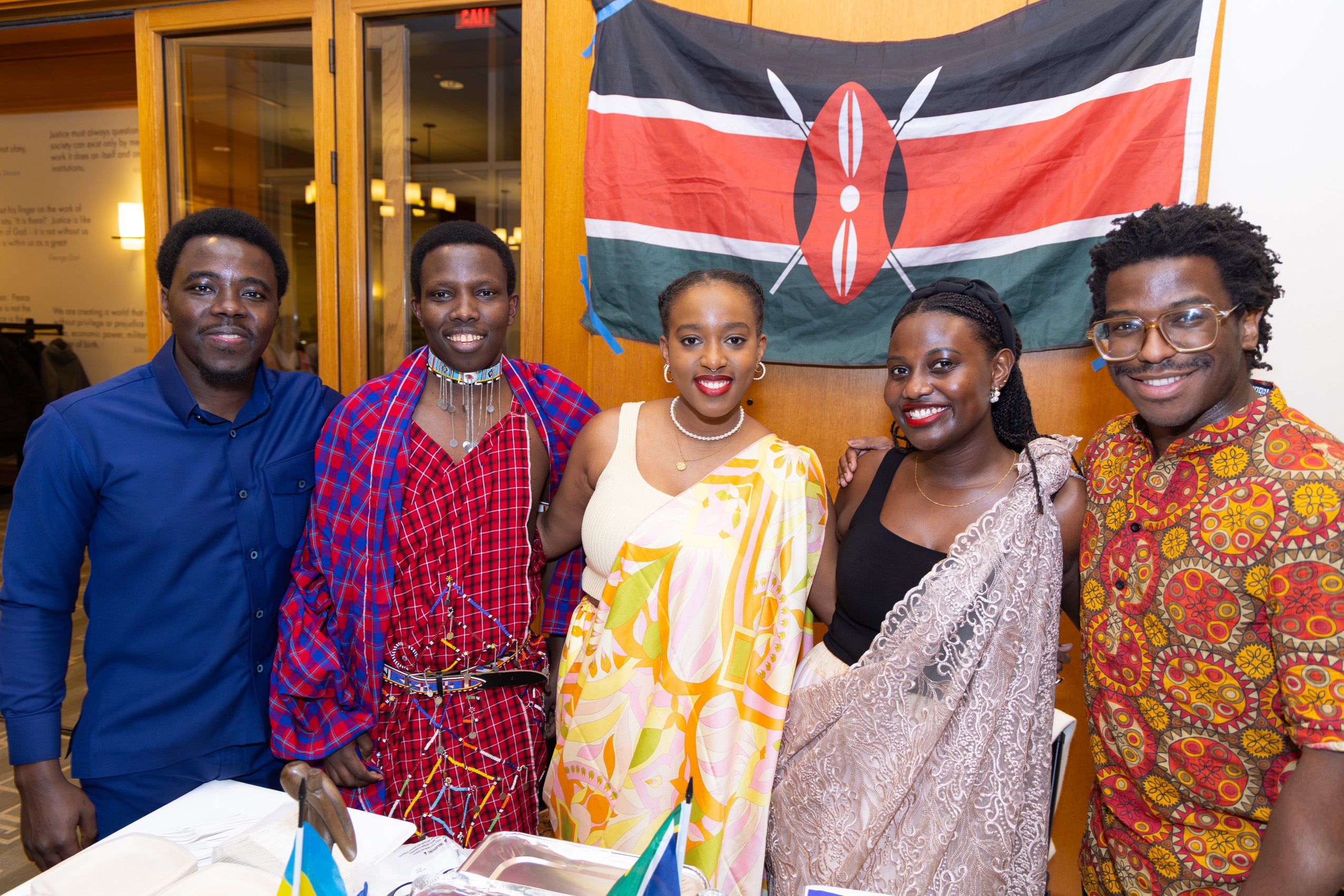 Five students wearing traditional dress from their homeland post in front of a flag.