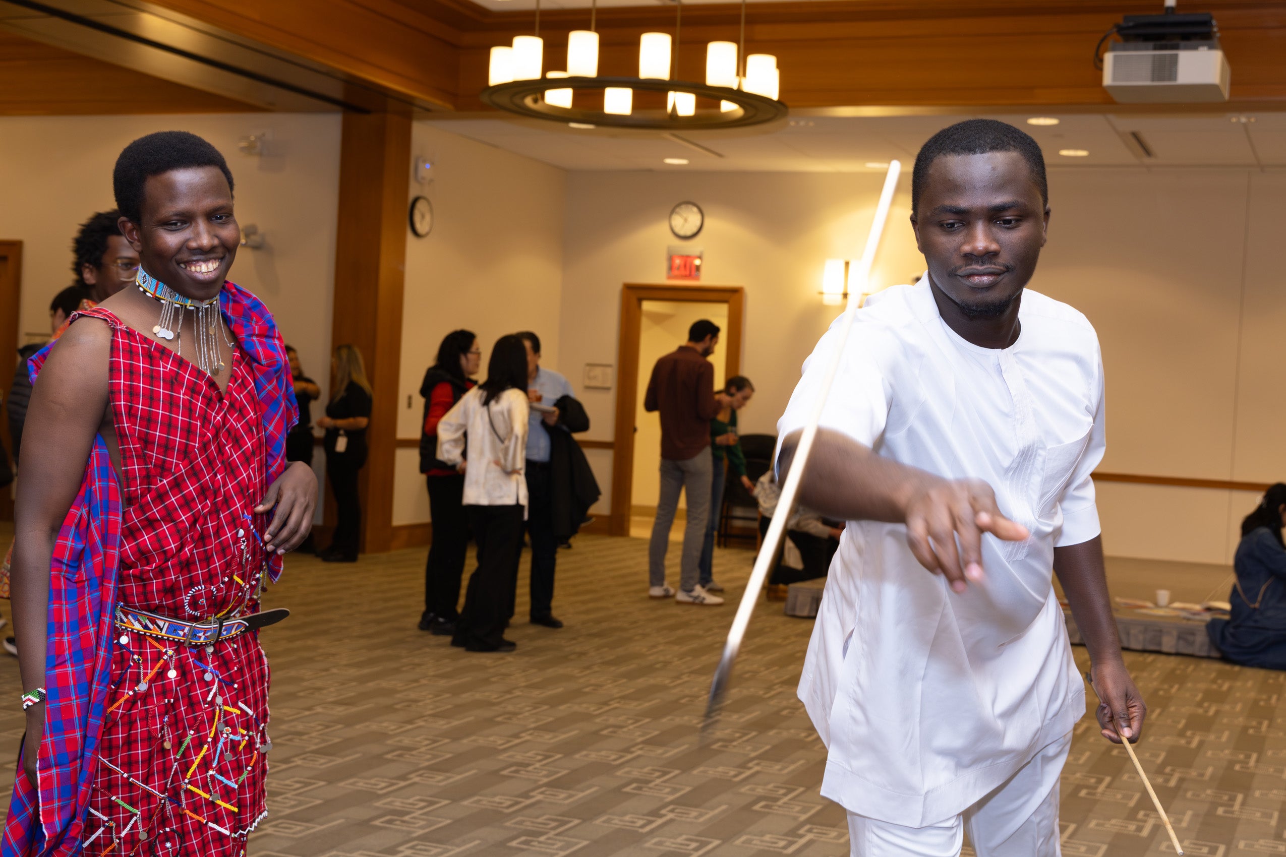 A man throws a stick at an international event while another man looks on.