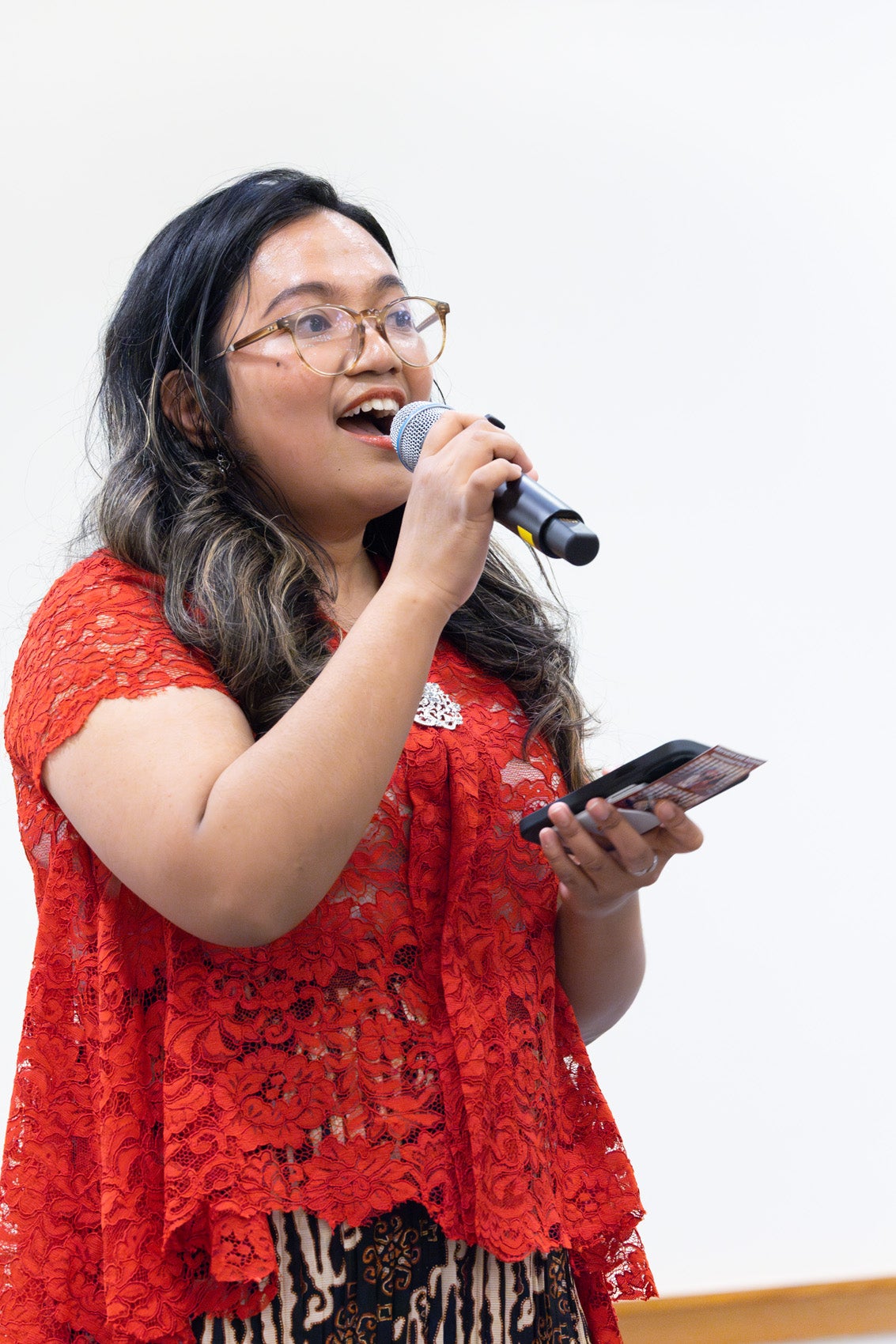 A woman in a red lace top holding a microphone.