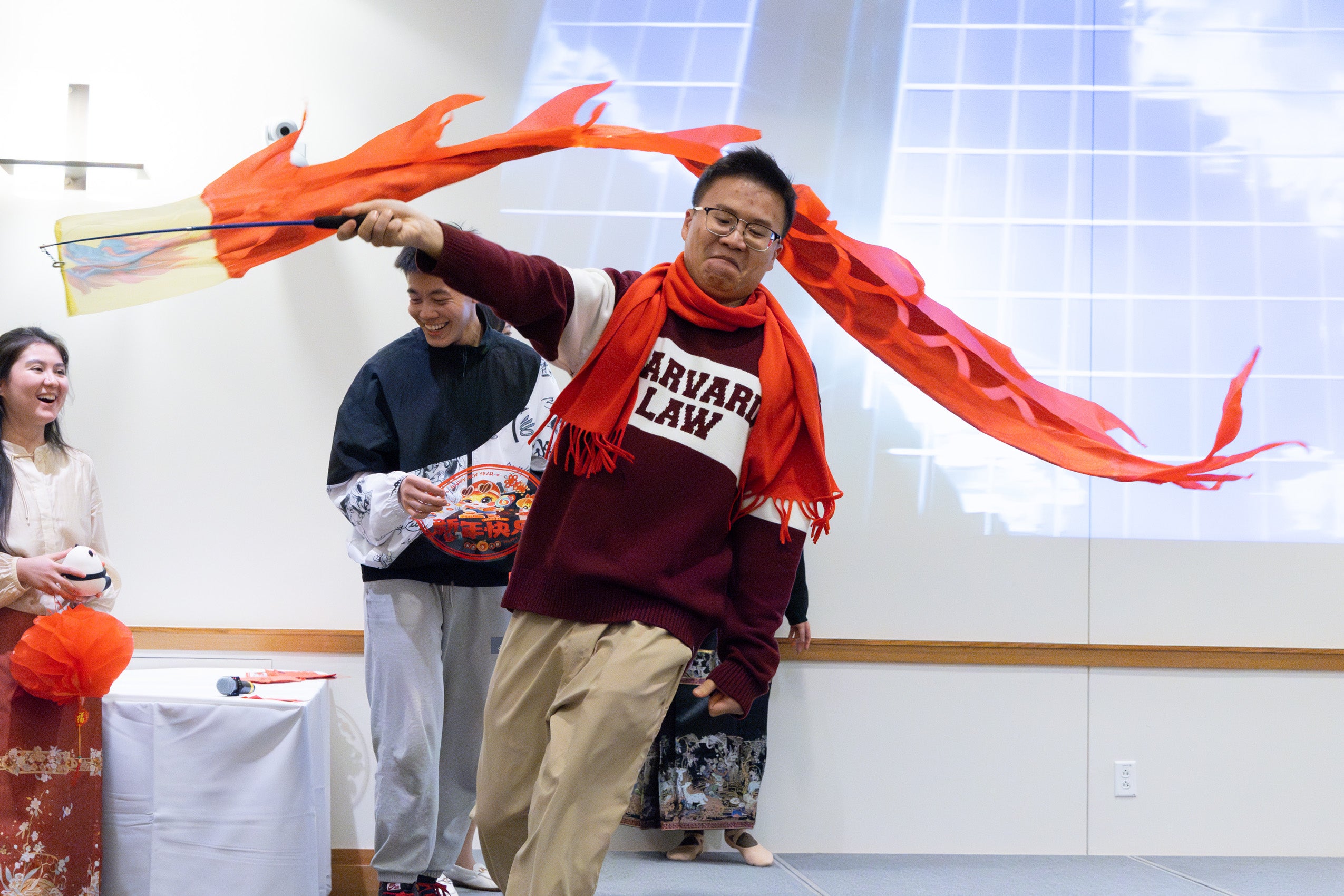 A man wearing a Harvard Law sweater runs along the stage with an orange dragon-like kite.