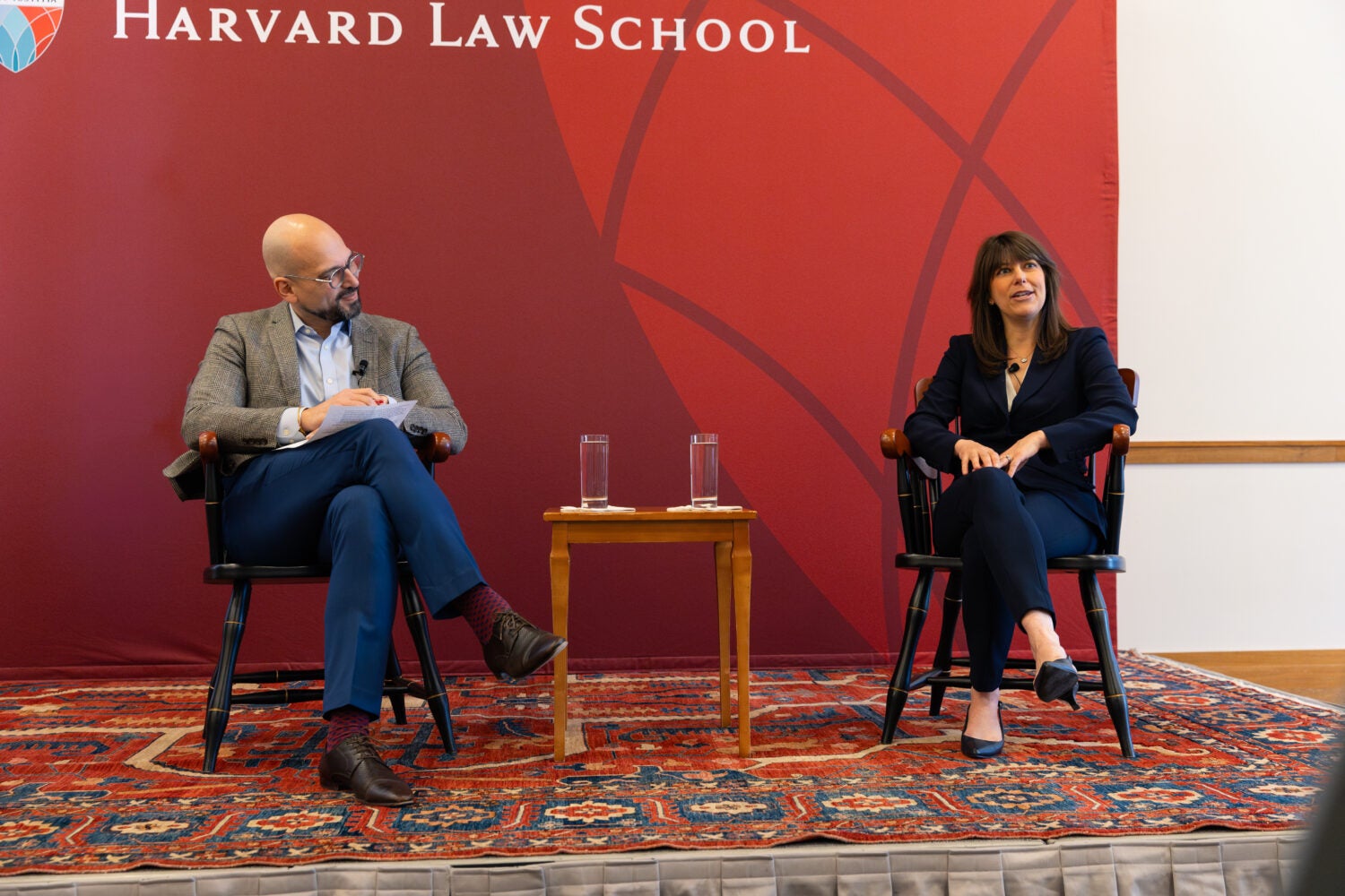 Man and woman sit in front of red backdrop.