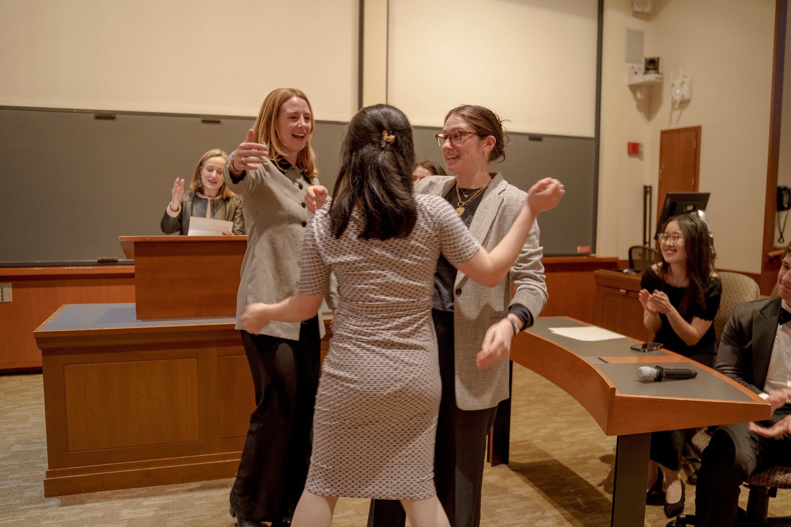 In a classroom three women congratulate each other as an announcement is made.